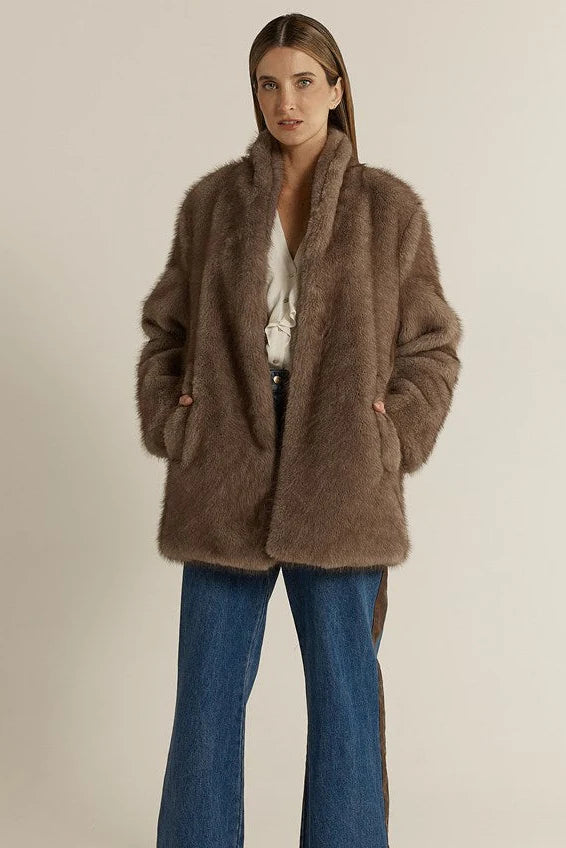 Woman wearing a Fate & Becker brown fluffy coat and blue jeans on a beige background