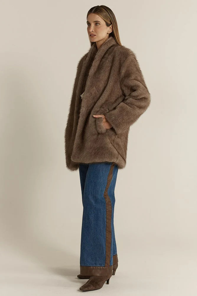 Woman wearing a Fate & Becker brown coat and blue jeans on a beige background