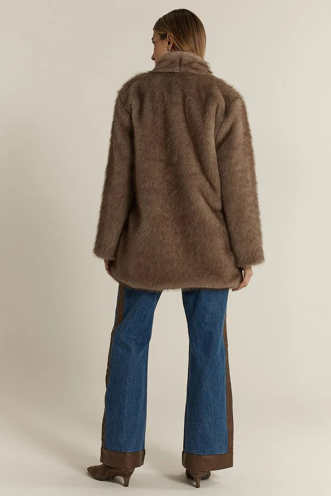 Image of Woman wearing a Fate and Becker brown coat and blue jeans on a beige background