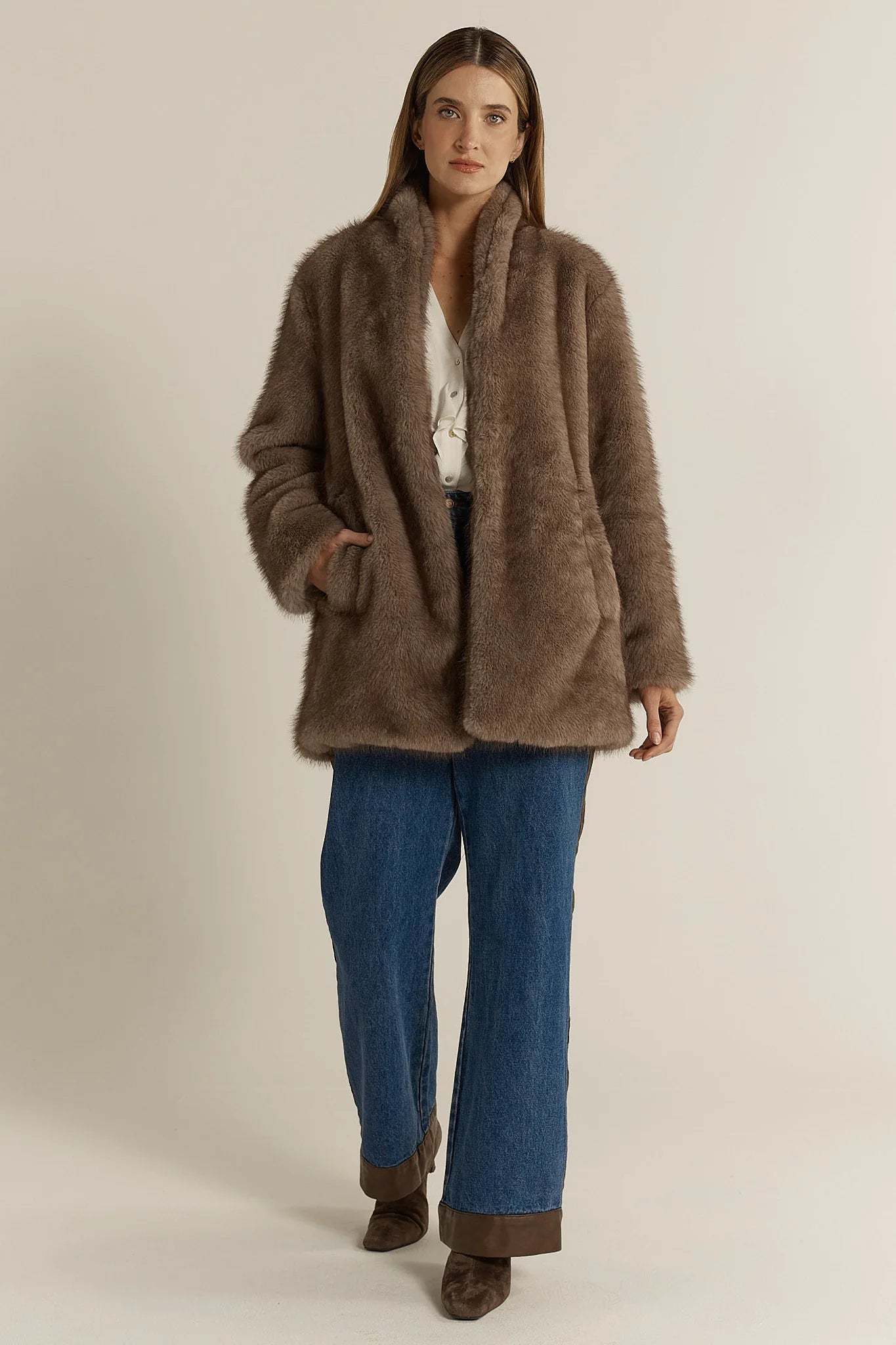 Woman wearing a Fate & Becker brown fur coat and blue jeans on a beige background