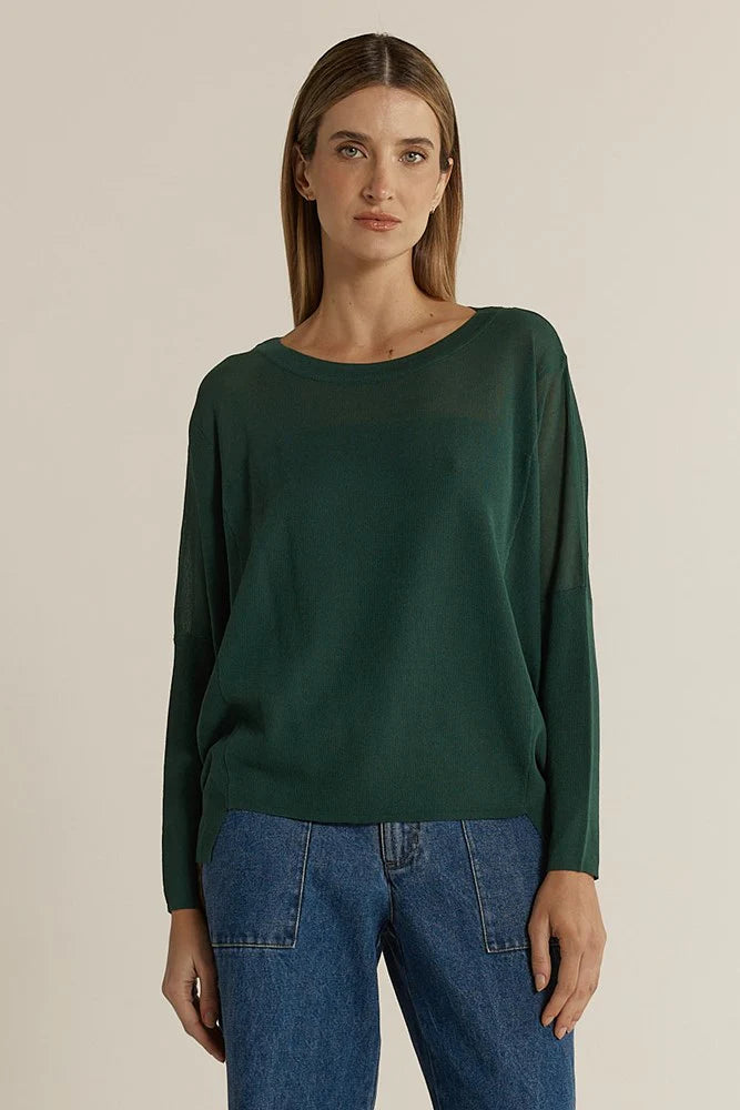 Image of Woman wearing a Fate & Becker dark green sweater and blue jeans against a beige background
