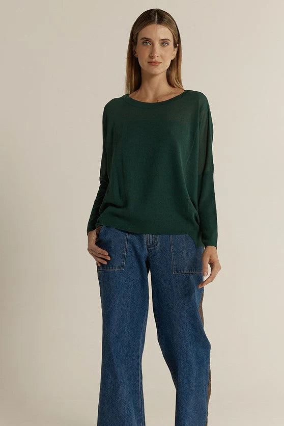 Image of Woman wearing a Fate & Becker dark green sweater and blue jeans against a beige background