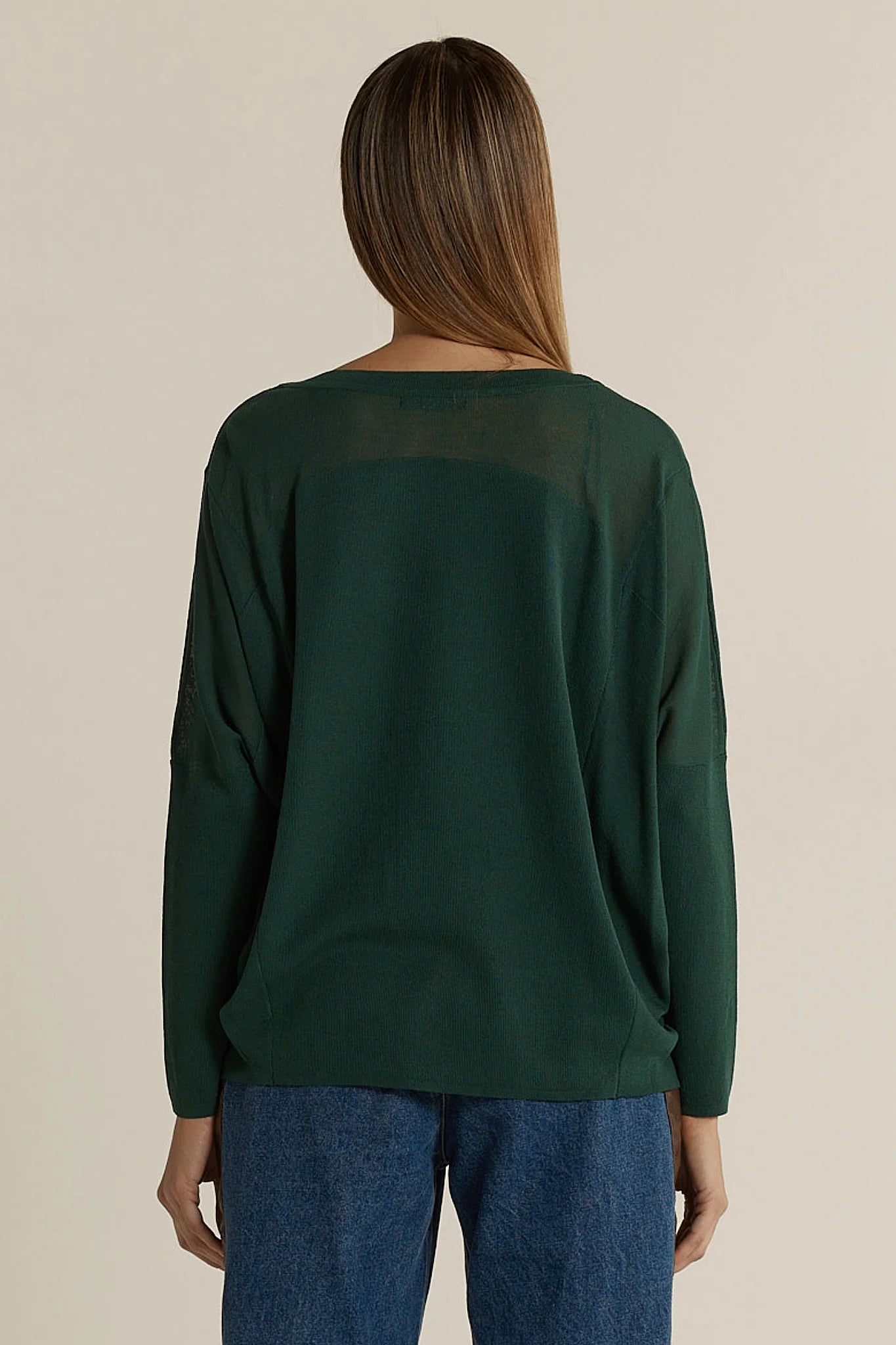 Image of Woman wearing a Fate & Becker green sweater and blue jeans on a beige background