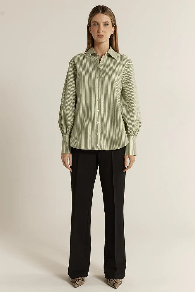 Image of Woman wearing a Fate & Becker green striped shirt and black pants on a beige background