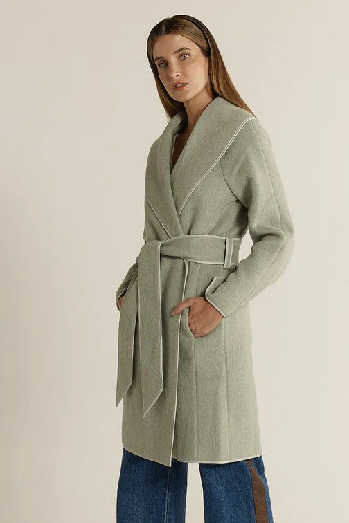 Image of Woman wearing a Fate & Becker light green coat with a belt on a plain background