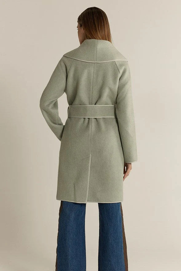Image of Woman wearing a Fate & Becker light green coat with a belt, standing against a plain background