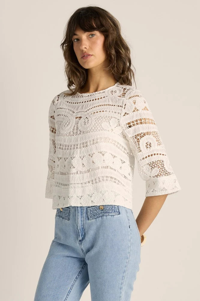 A woman wearing a Betty Basics white crochet lace top with three-quarter sleeves and light blue jeans, photographed against a plain light beige studio background.