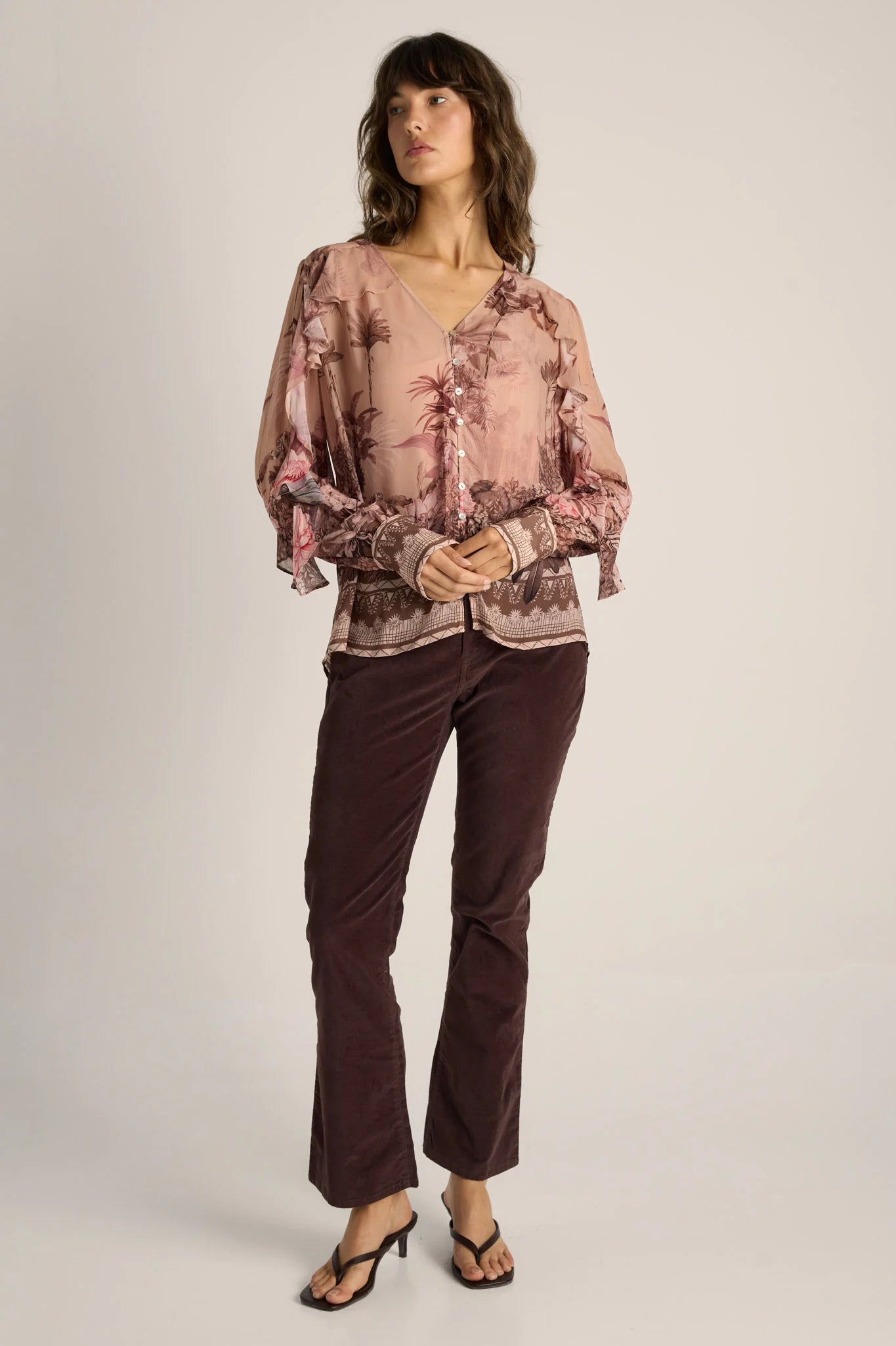 Image of Woman wearing a Fate & Becker patterned blouse and brown pants on a plain background