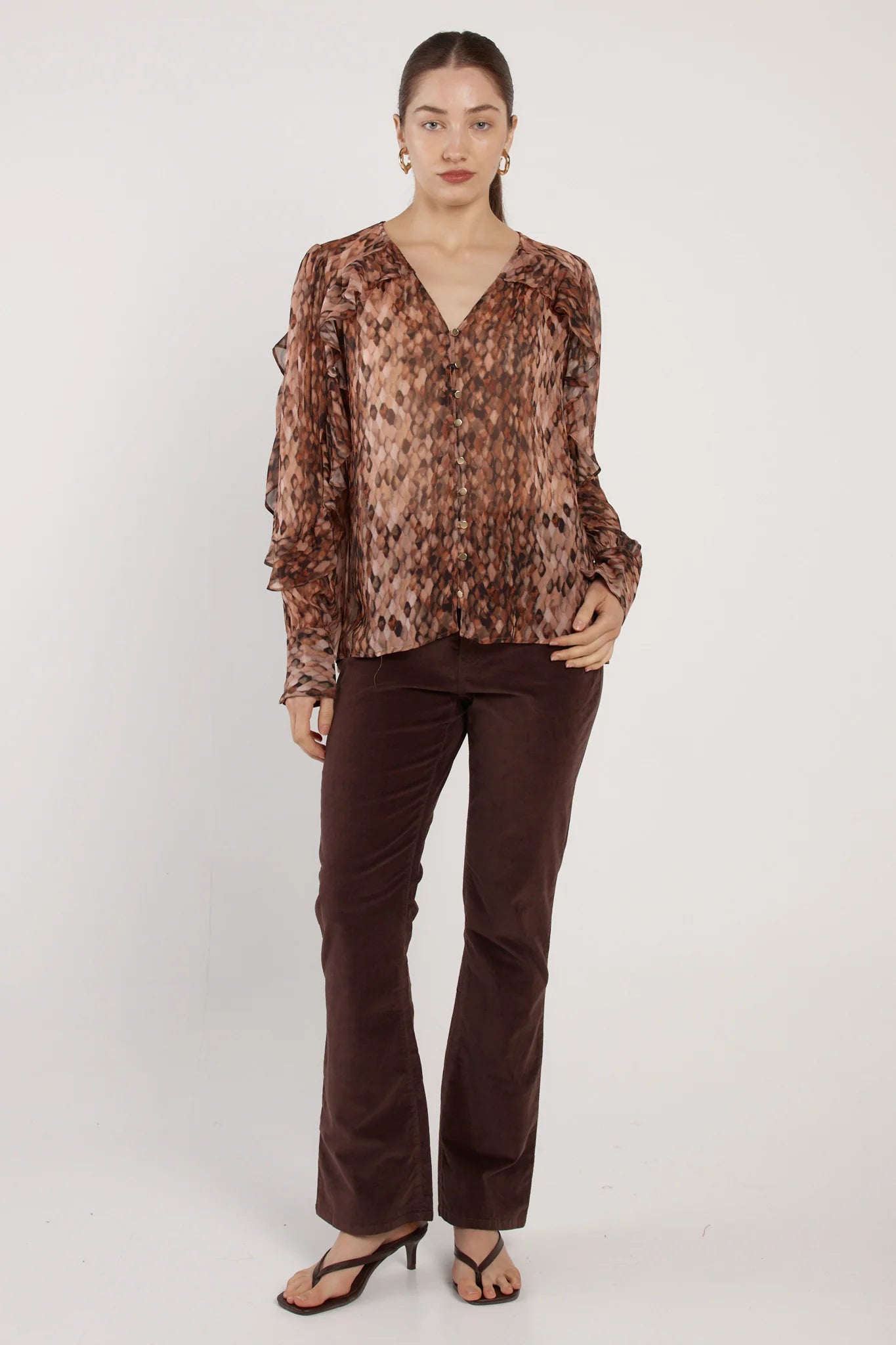 Image of Woman wearing a Fate & Becker patterned blouse and brown pants on a white background