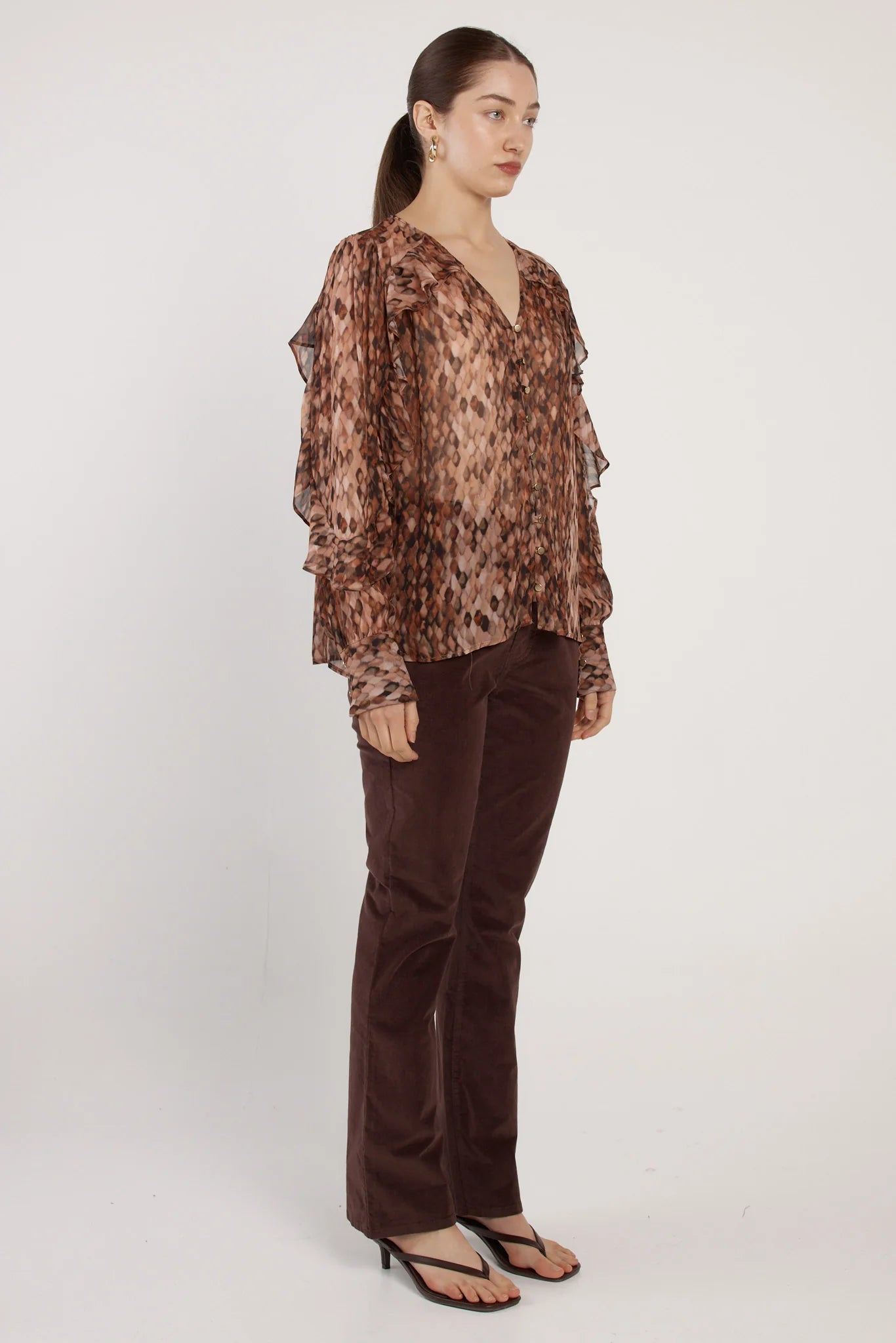 Woman wearing a Fate & Becker brown patterned blouse and brown pants on a white background