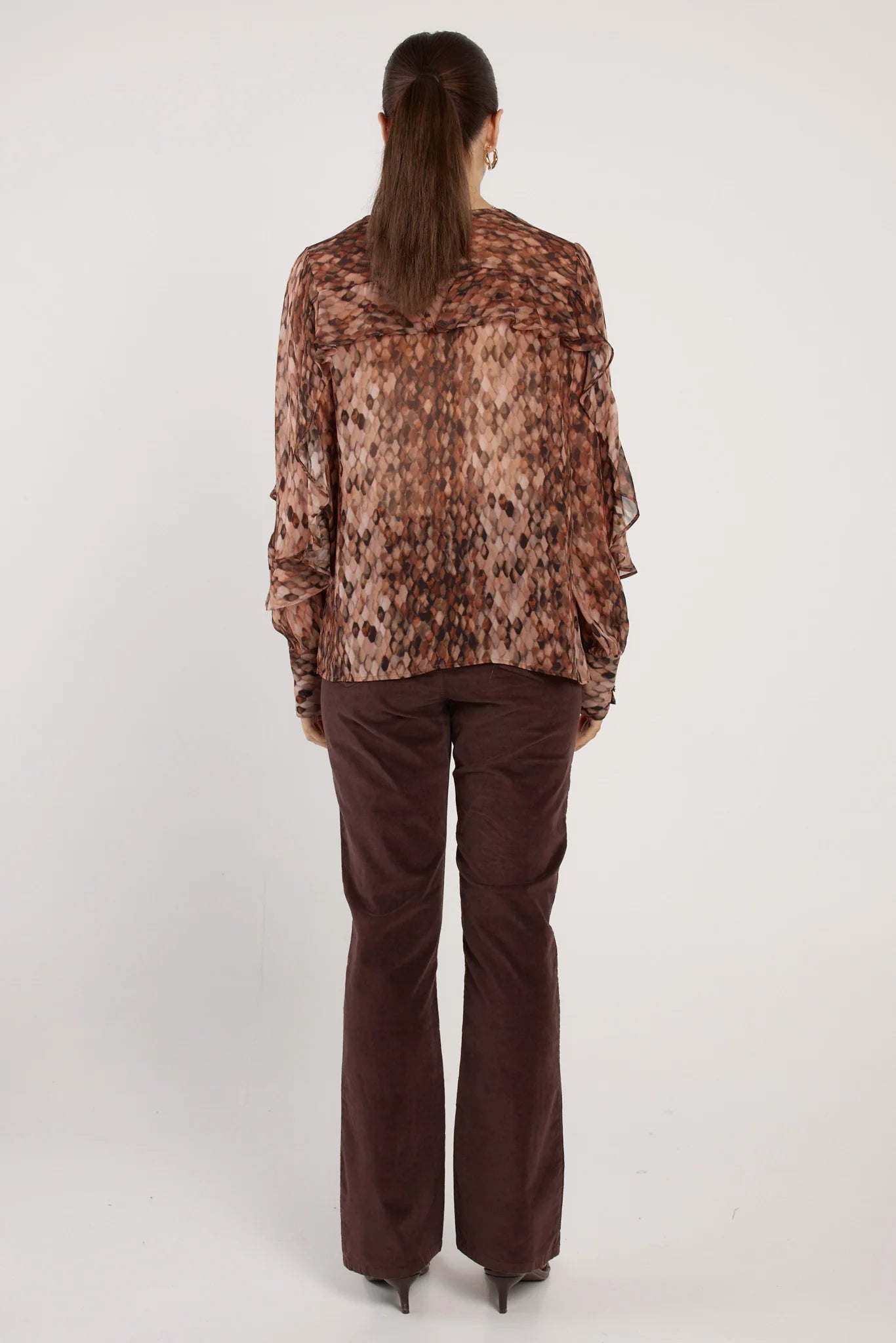 Woman wearing a Fate & Becker patterned blouse and brown pants on a white background