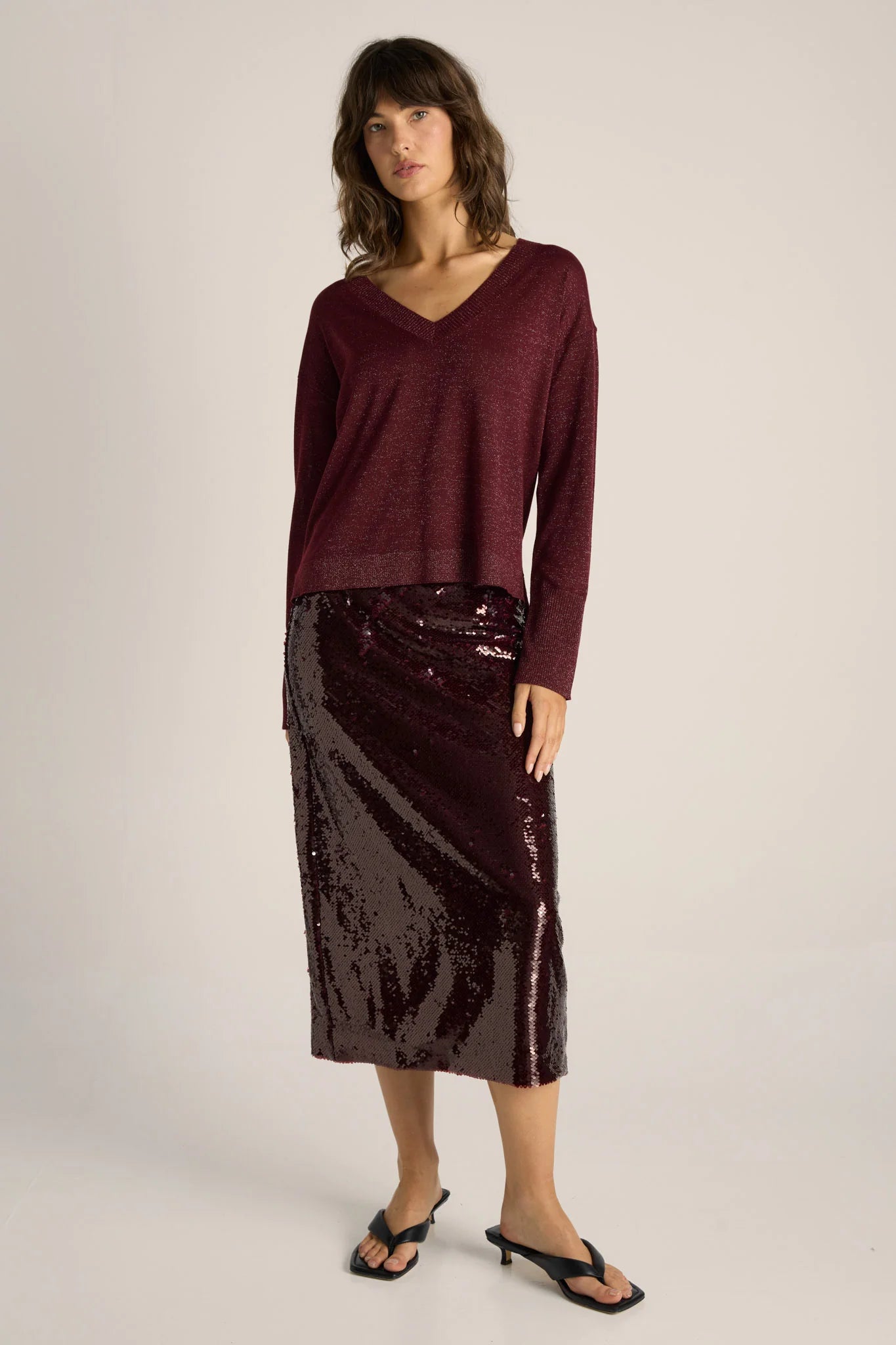 Image of Woman wearing a Fate & Becker burgundy sweater and sequin skirt on a plain background