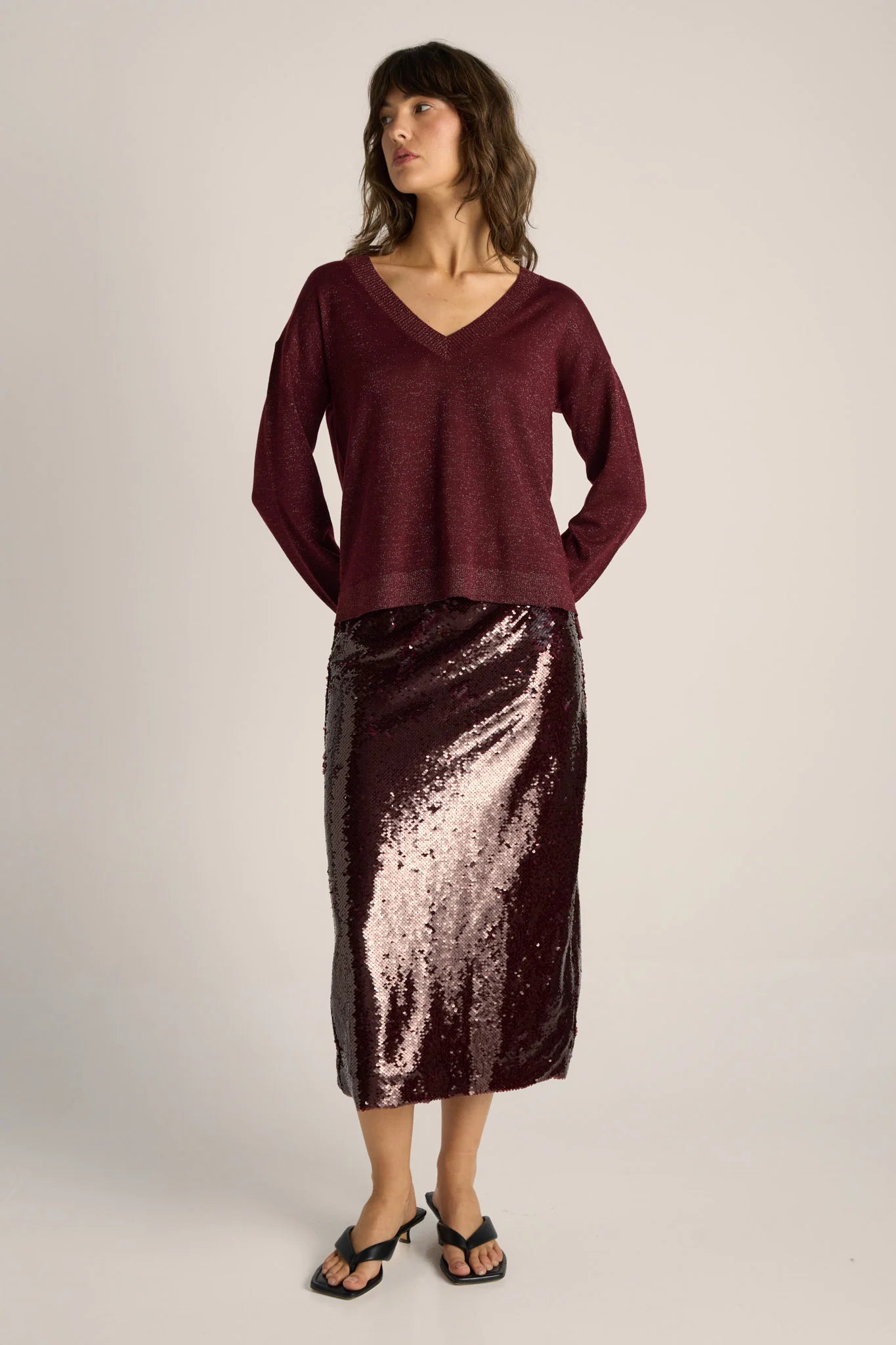 Image of Woman wearing a Fate & Becker burgundy sweater and sequin skirt on a plain background
