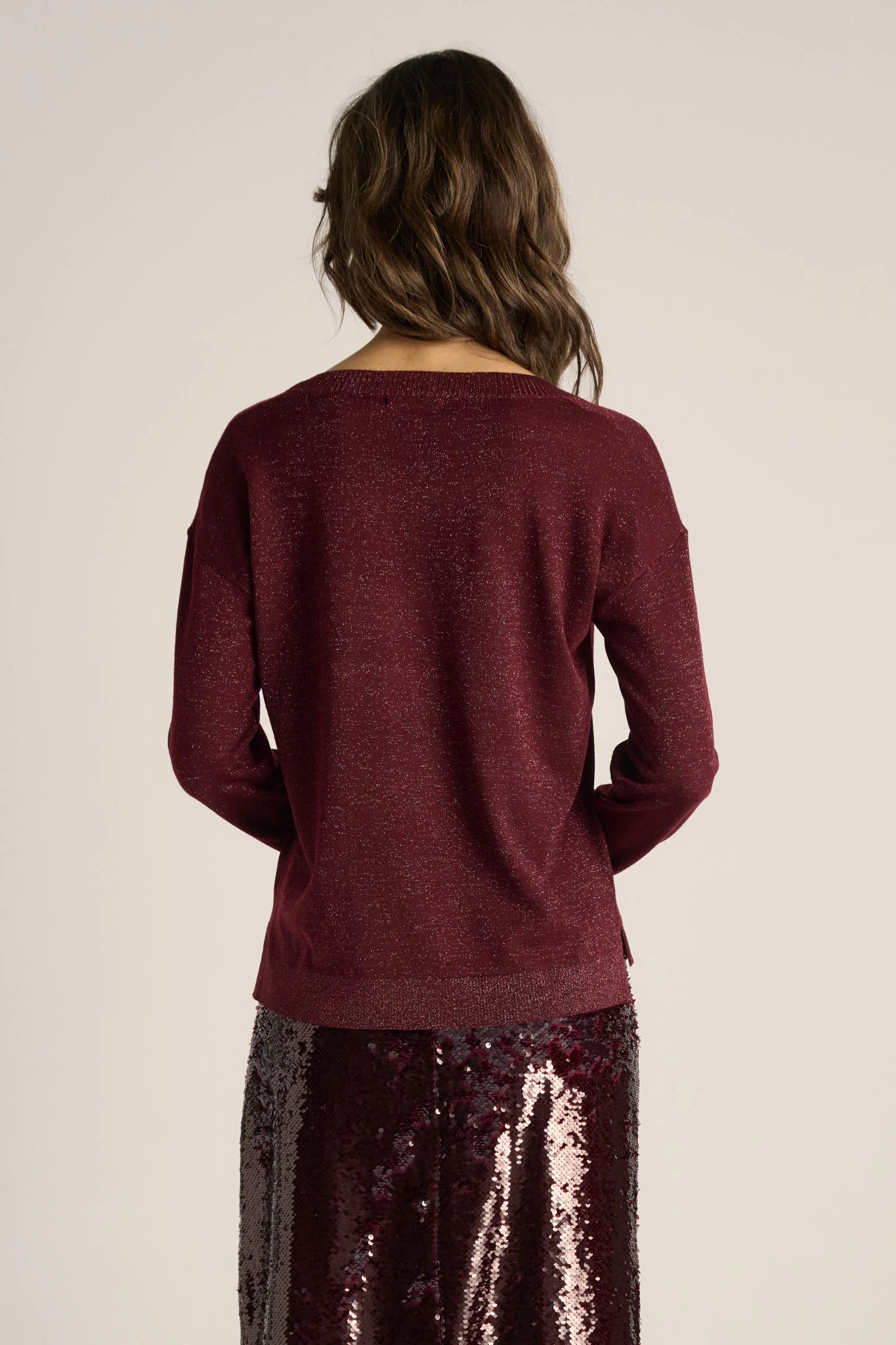Woman wearing a Fate & Becker burgundy sweater and sequin skirt on a beige background