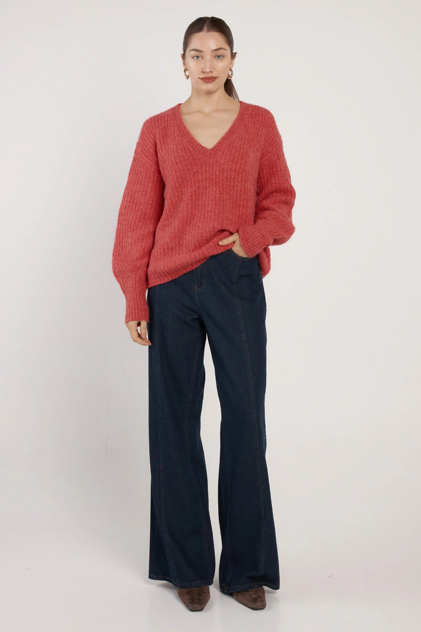 Woman wearing a Fate and Becker red sweater and dark blue pants on a white background
