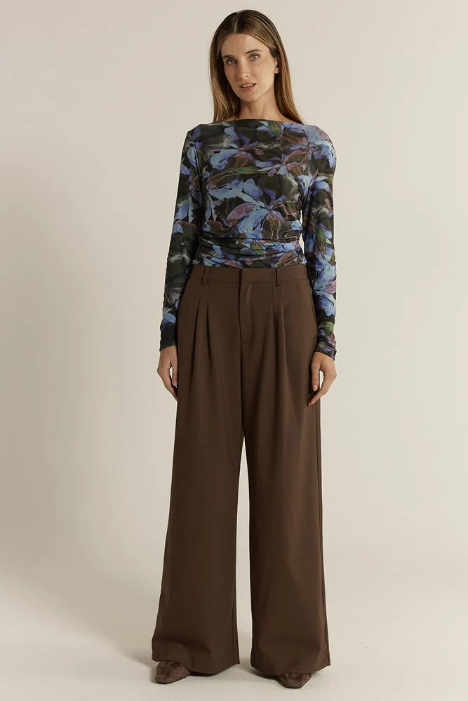 Woman wearing a patterned top and Fate & Becker brown wide-leg pants on a beige background