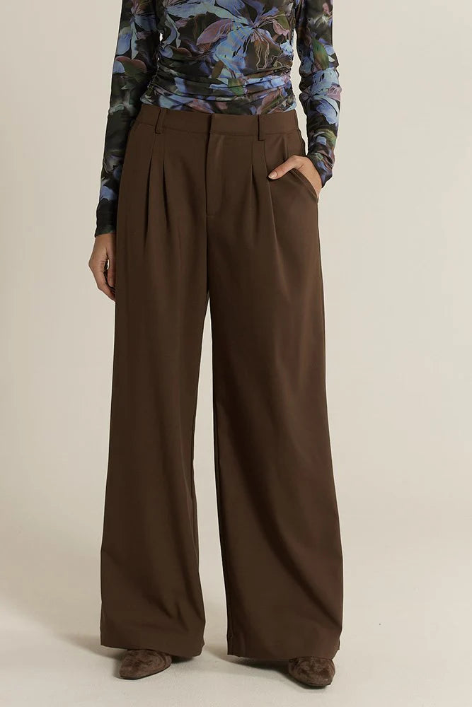 Fate & Becker brown wide-leg pants worn with a patterned top on a beige background