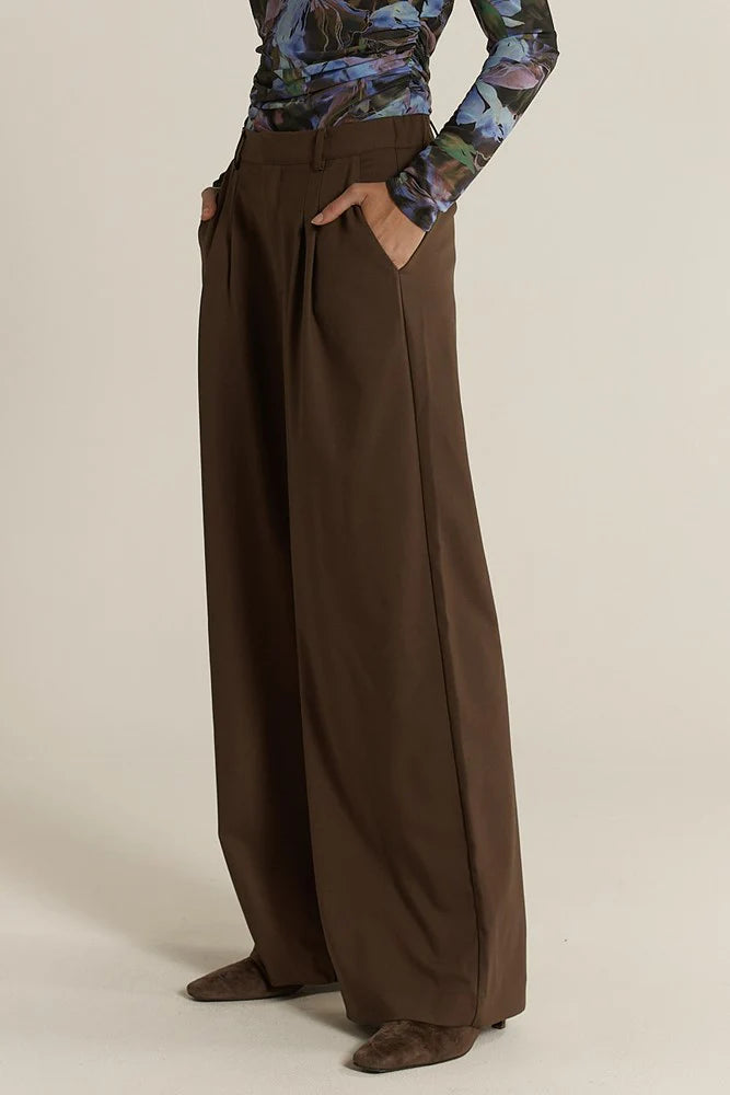 Fate & Becker brown wide-leg pants worn by a woman on a beige background