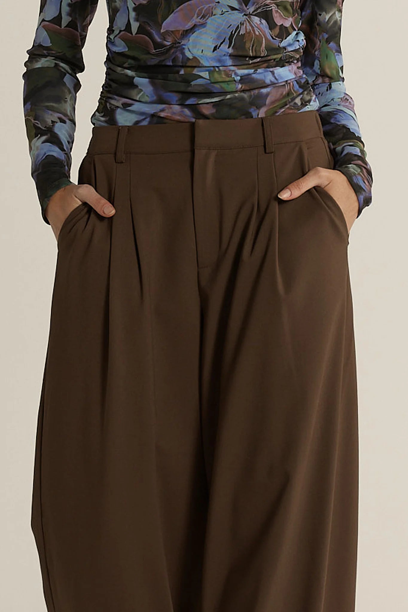 Woman wearing a floral long-sleeve top and Fate & Becker brown wide-leg pants on a beige background