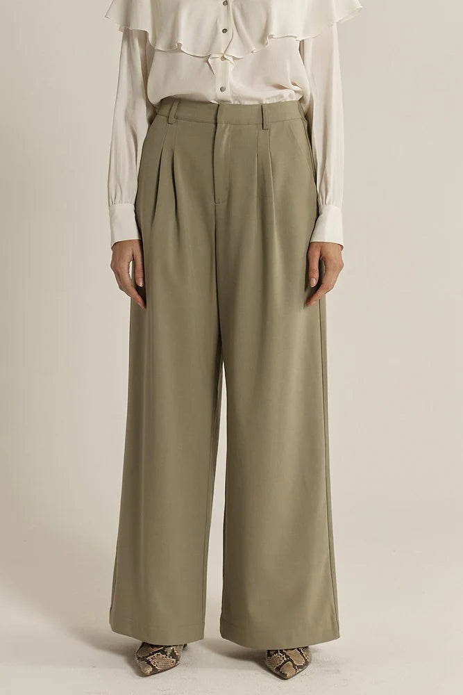 Woman wearing sage Fate & Becker wide-leg pants and a white blouse on a plain background