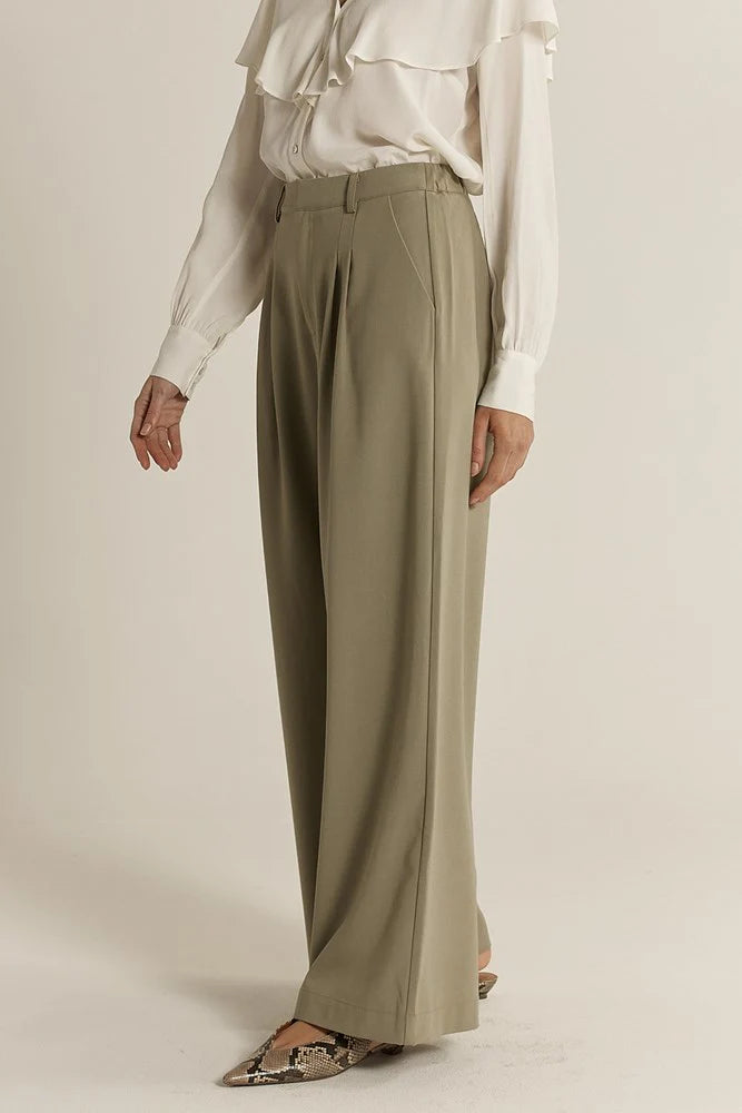 Woman wearing a white blouse and sage Fate & Becker wide-leg pants on a plain background