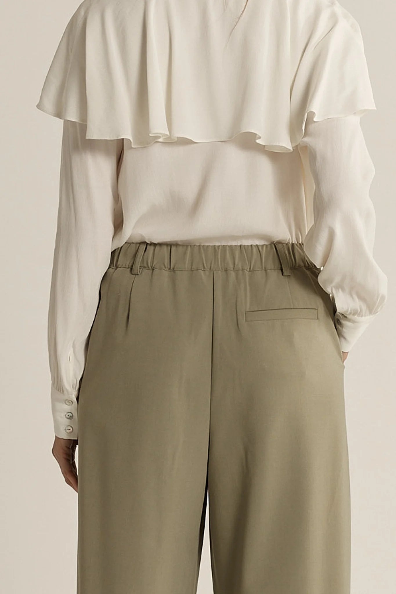 Image of Woman wearing a white blouse and sage Fate & Becker pants against a neutral background