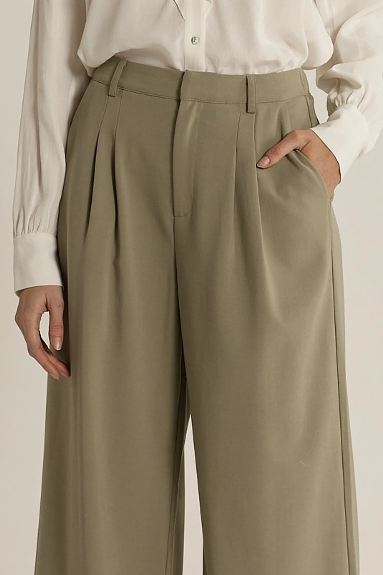 Image of Woman wearing Fate & Becker olive green pleated pants with a white shirt on a beige background