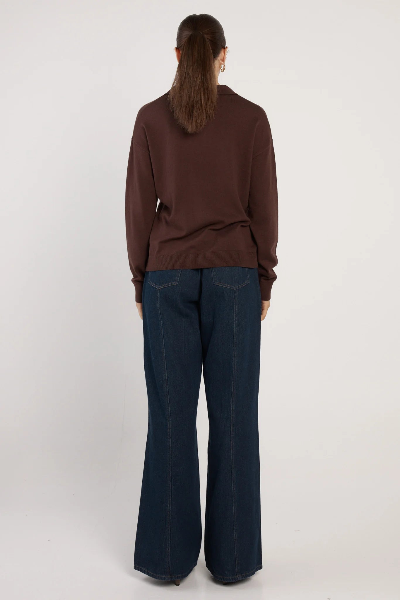 Woman wearing a Fate and Becker brown sweater and dark blue jeans on a white background