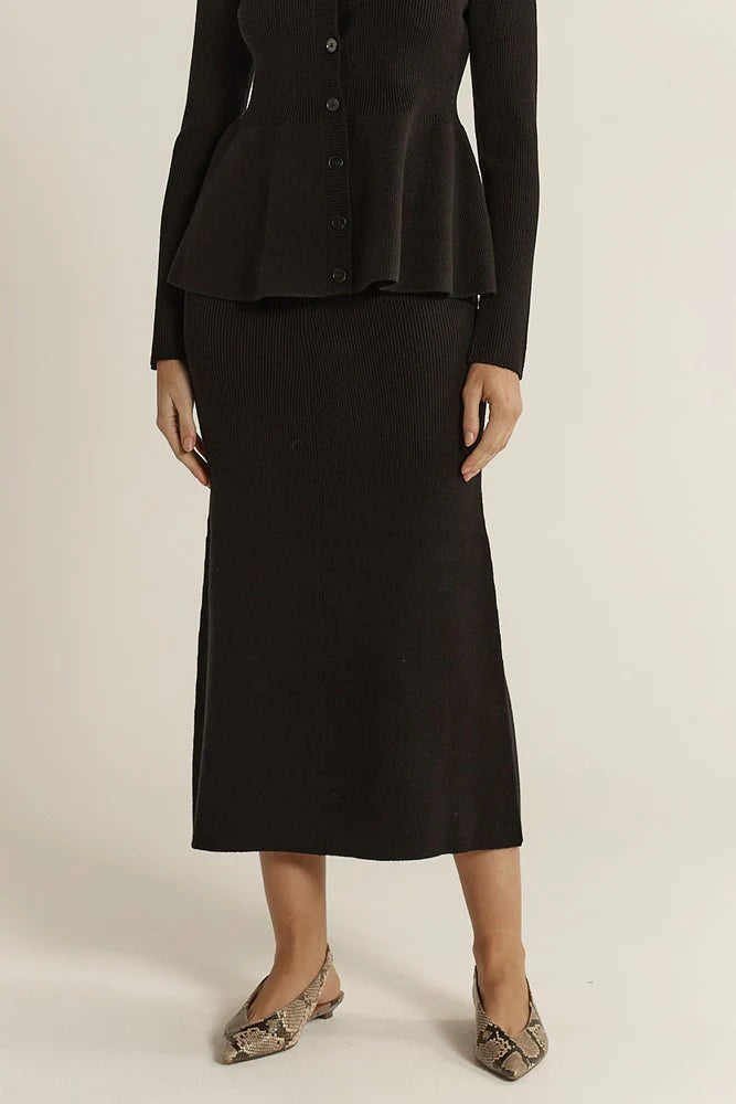Woman wearing a Fate & Becker black suit with a skirt on a beige background