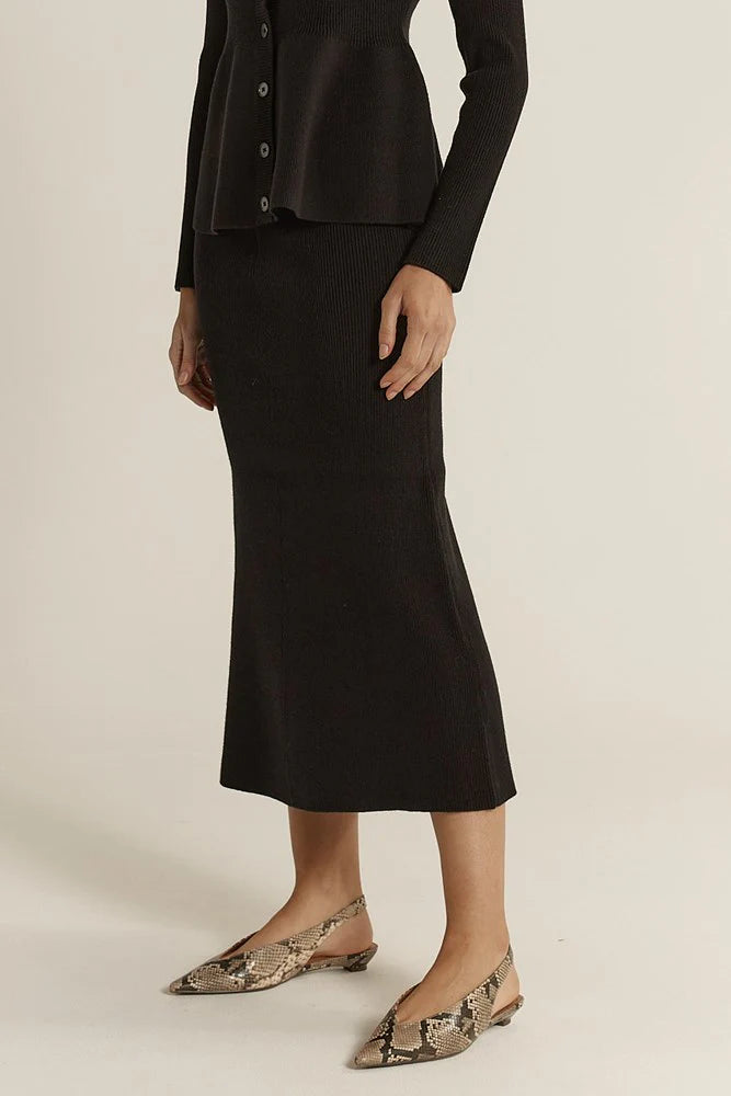 Image of Woman wearing a Fate & Becker black outfit with a skirt and snake print shoes on a neutral background