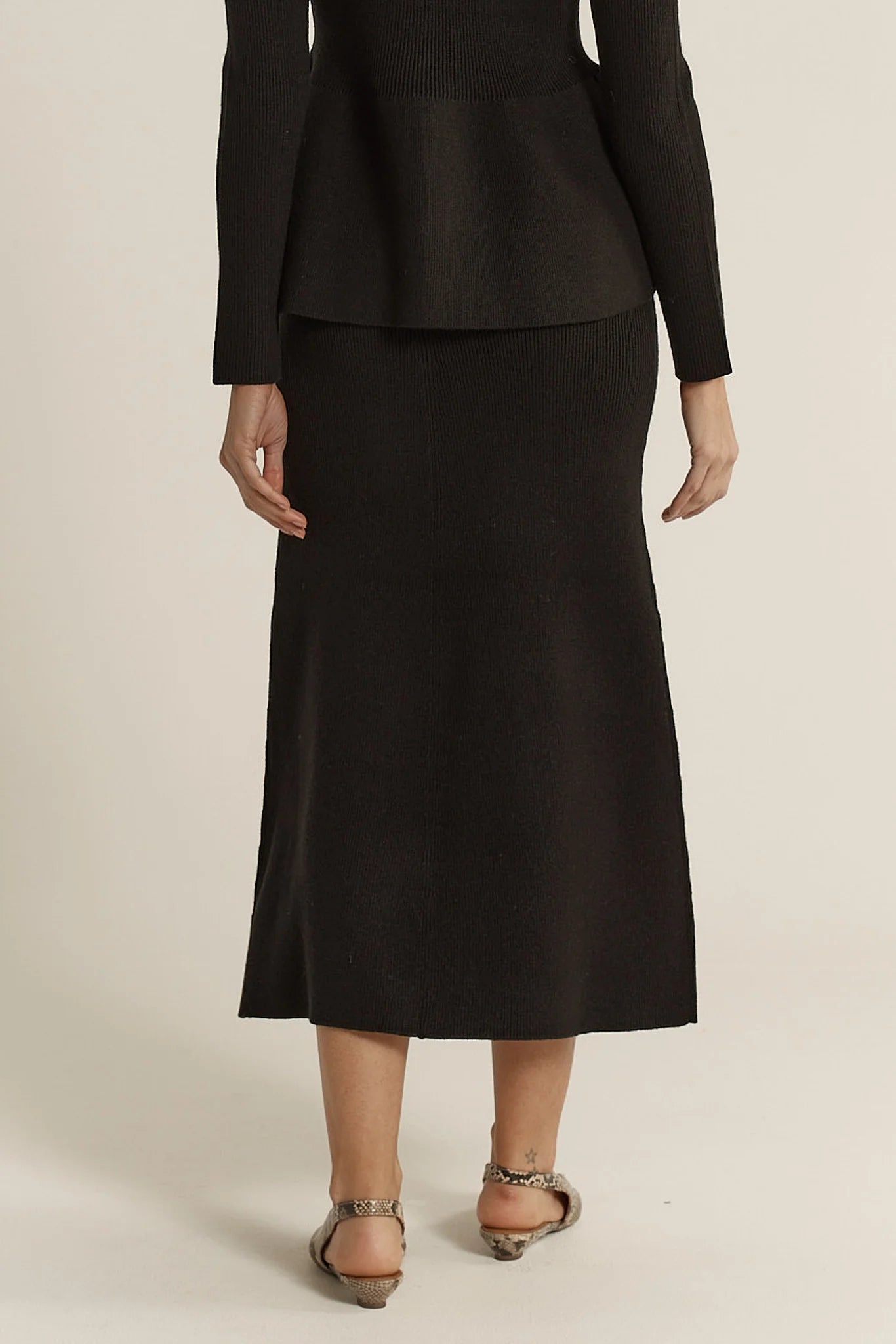 Image of Woman wearing a Fate & Becker black suit with a skirt on a beige background
