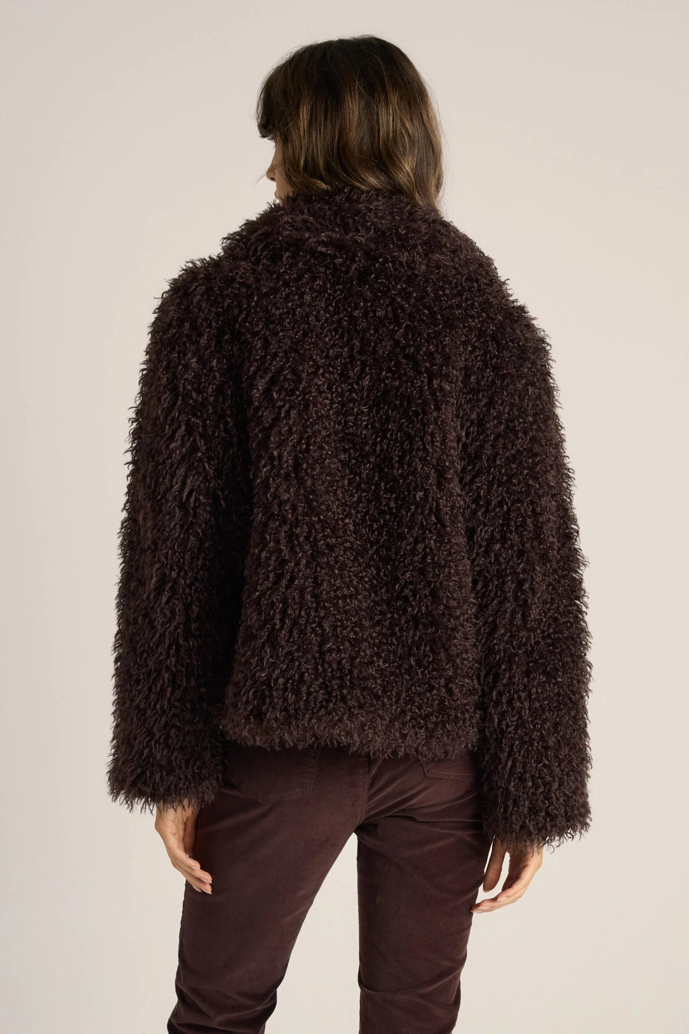 Woman wearing a Fate & Becker dark brown fluffy jacket on a plain background