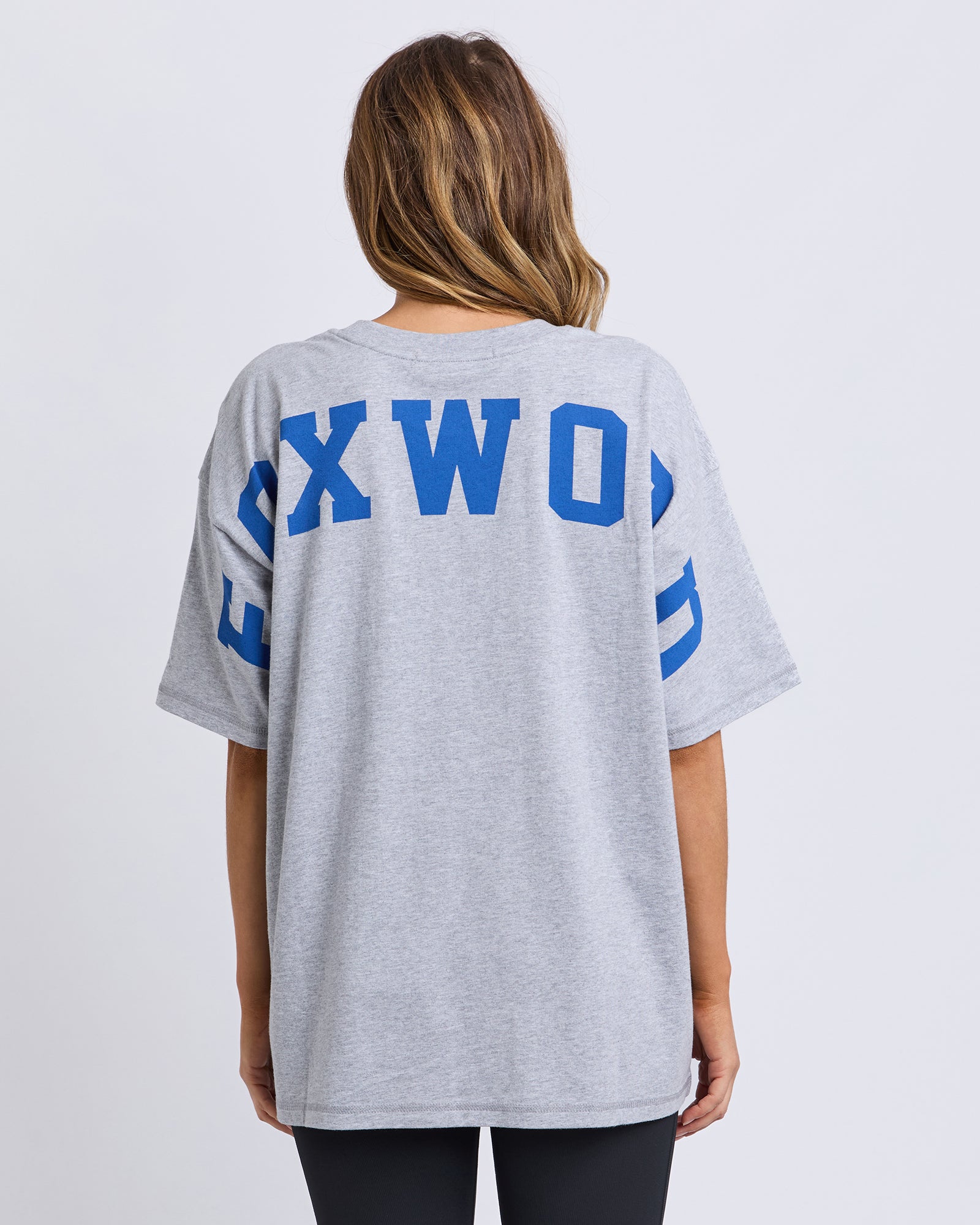 Woman wearing a Foxwood grey t-shirt with blue text on the back against a white background