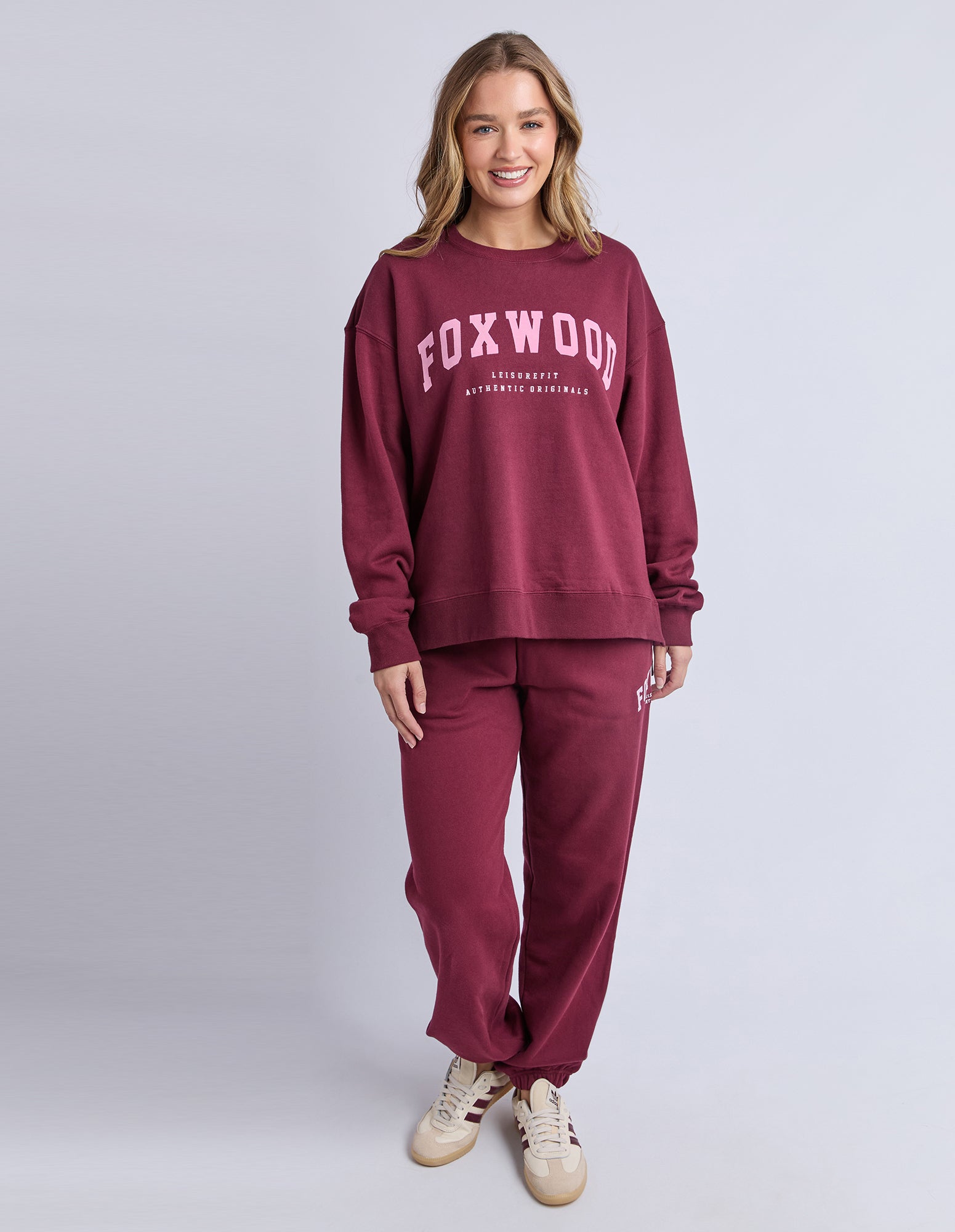 Woman wearing a maroon 'FOXWOOD' jumper and pants on a light grey background