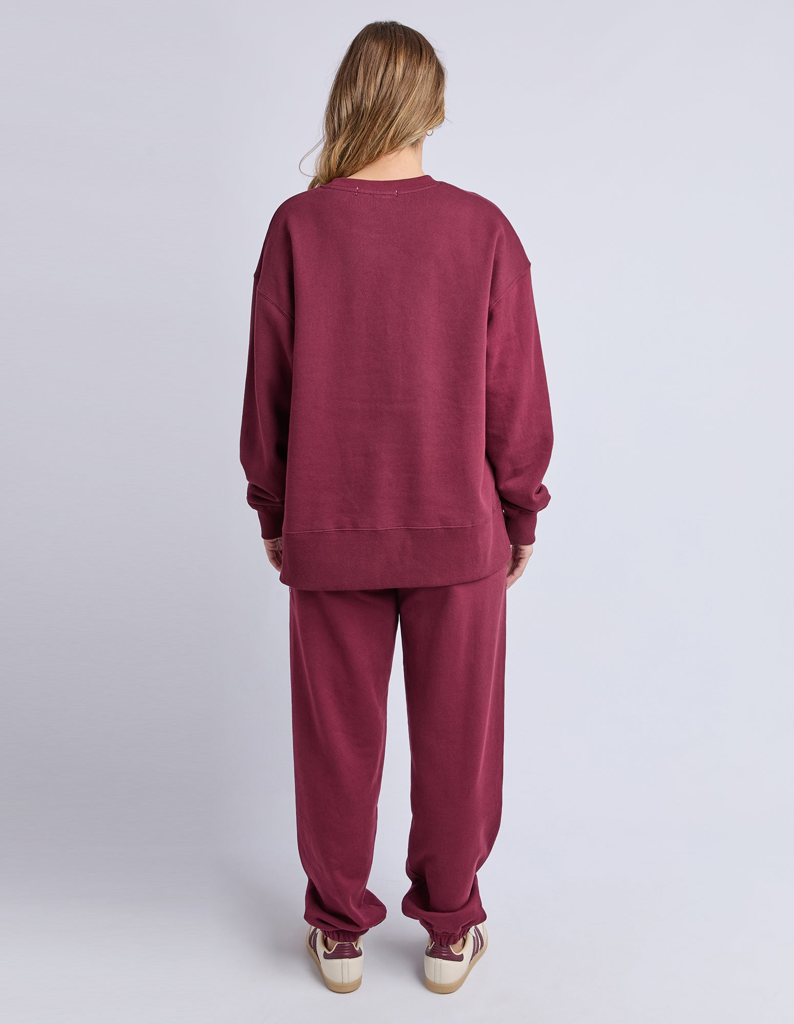 Image of Backview of a woman wearing a burgundy jumper and pants on a light grey background