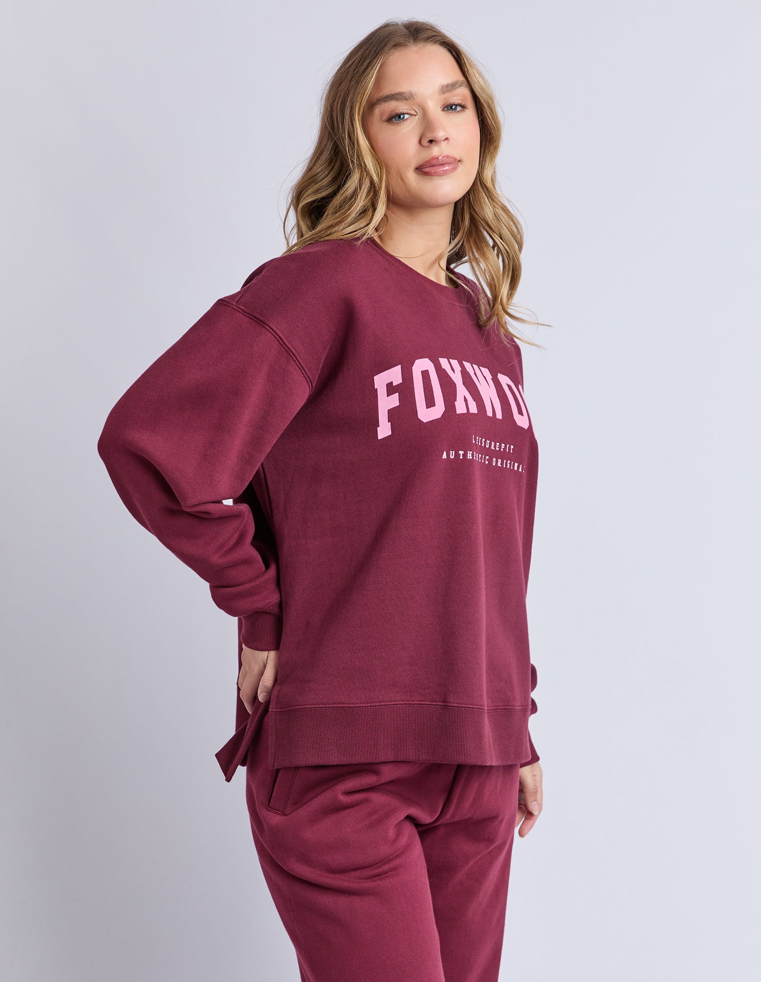 Image of Woman wearing a maroon jumper with 'FOXWOOD' branding on a light grey background