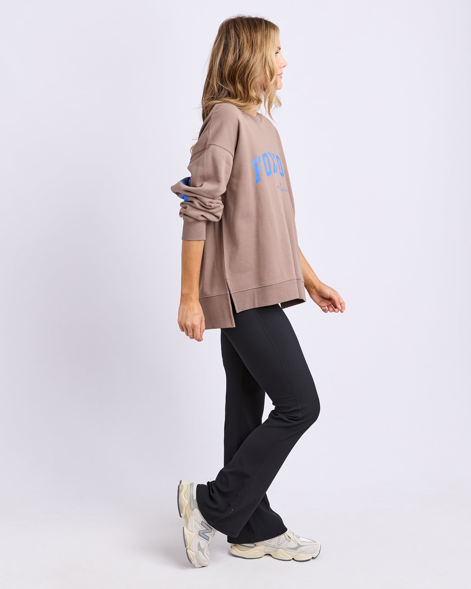 Collection of Side view of a Woman wearing a Foxwood brown jumper with blue text and black pants on a white background in a gallery layout