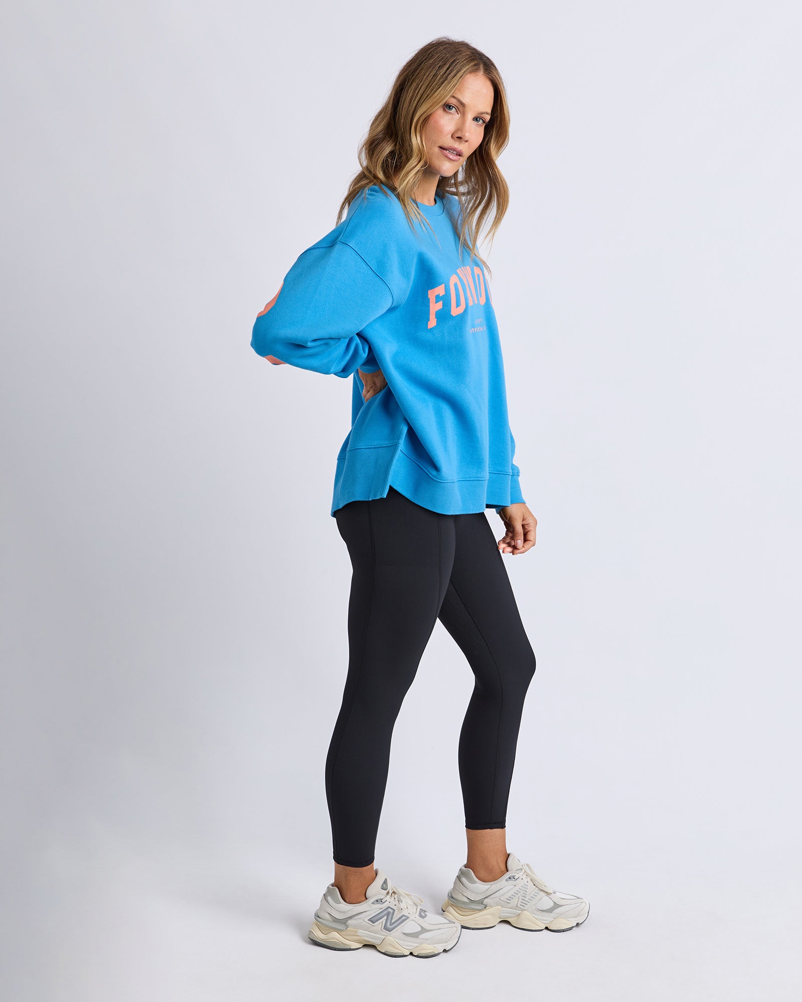 Image of Woman wearing a blue Foxwood bright blue jumper with 'FOXWOOD' branding and black leggings on a white background