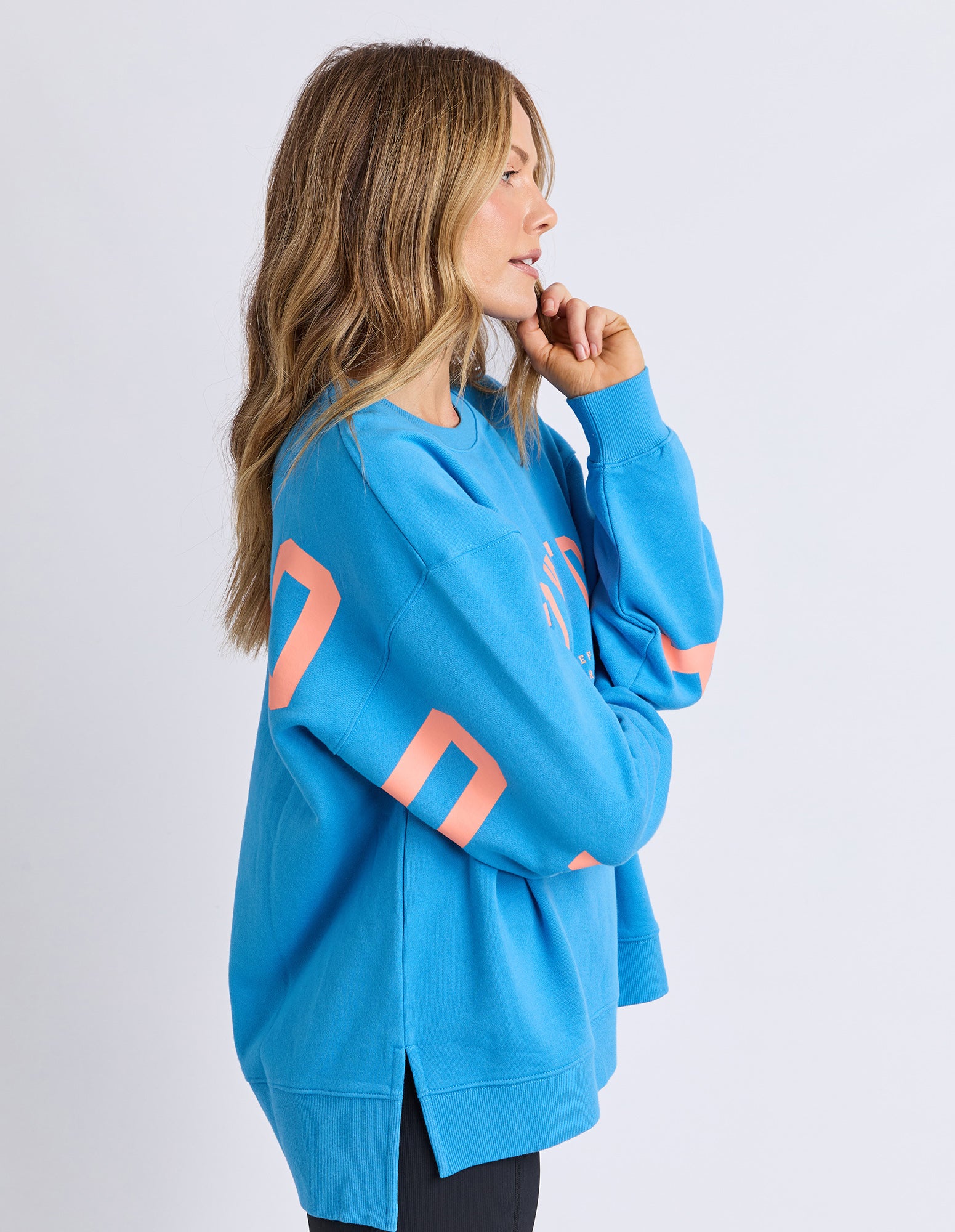 Image of Sideview of a woman wearing a Foxwood bright blue jumper with orange lettering on a white background
