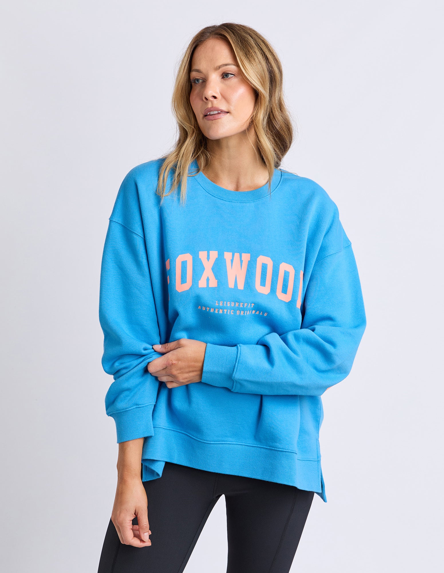 Image of Woman wearing a Foxwood bright blue sweatshirt with 'FOXWOOD' printed on it in orange against a white background