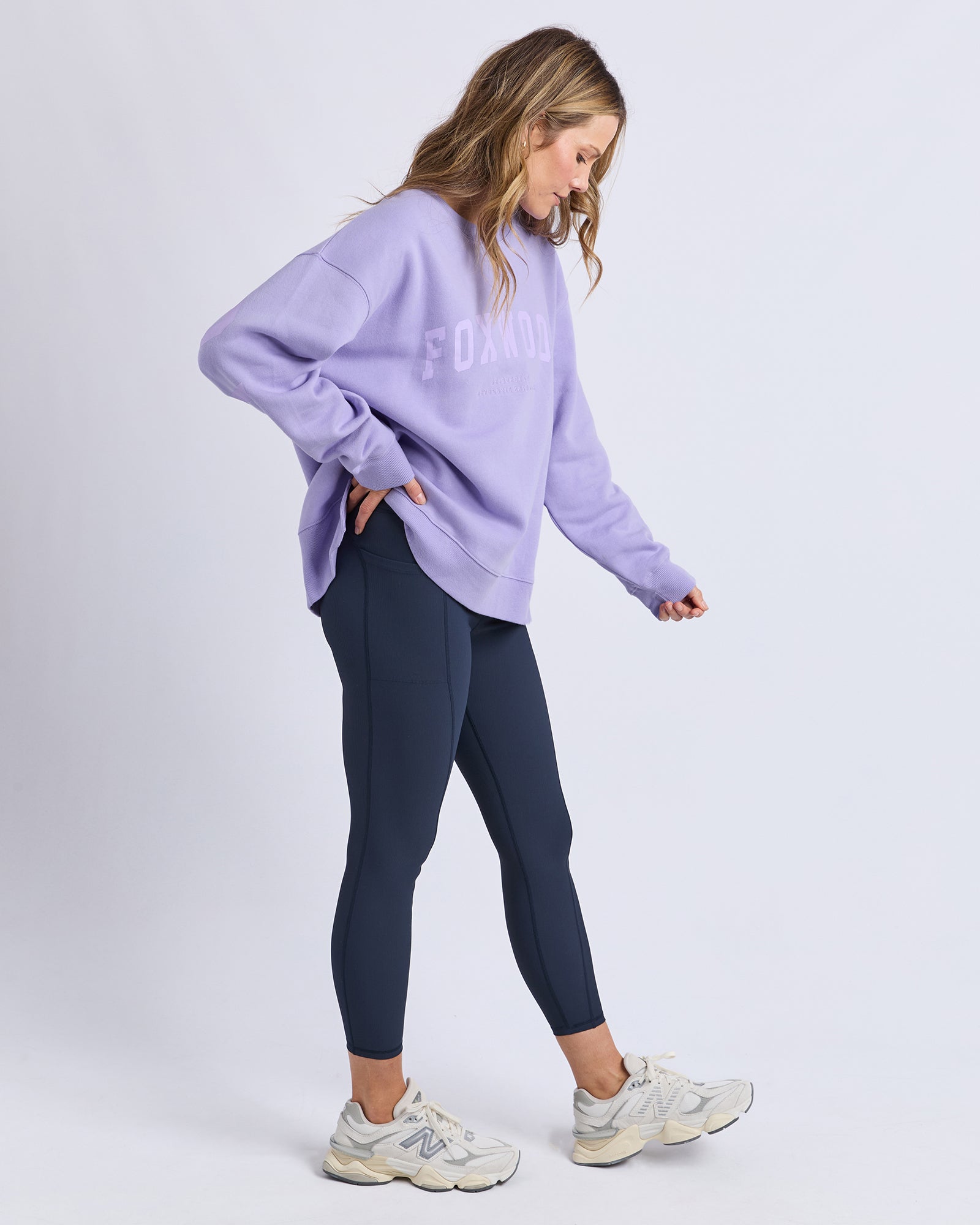 Woman wearing a light purple /lavender jumper and dark blue leggings on a white background