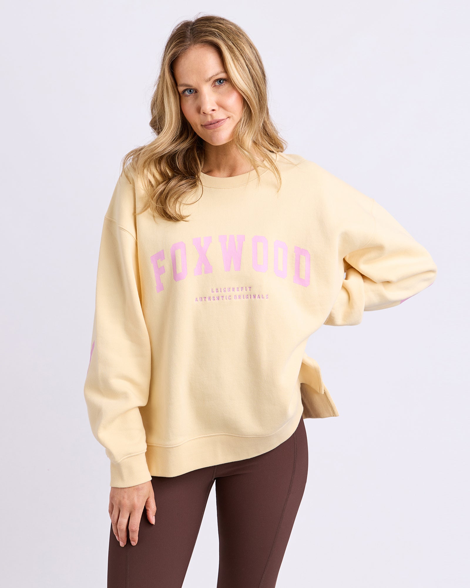 Image of Woman wearing a Foxwood light yellow sweatshirt with 'FOXWOOD' printed in pink on a white background