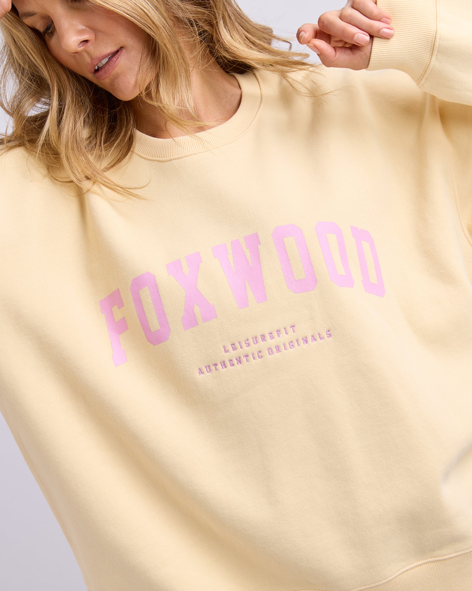 Image of Light yellow jumper with pink 'FOXWOOD' text worn by a person on a light grey background