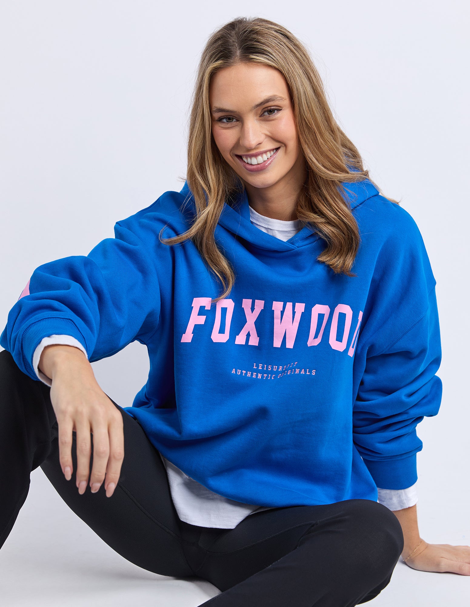 Woman wearing a blue hoodie with 'FOXWOOD' branding in pink on a white background