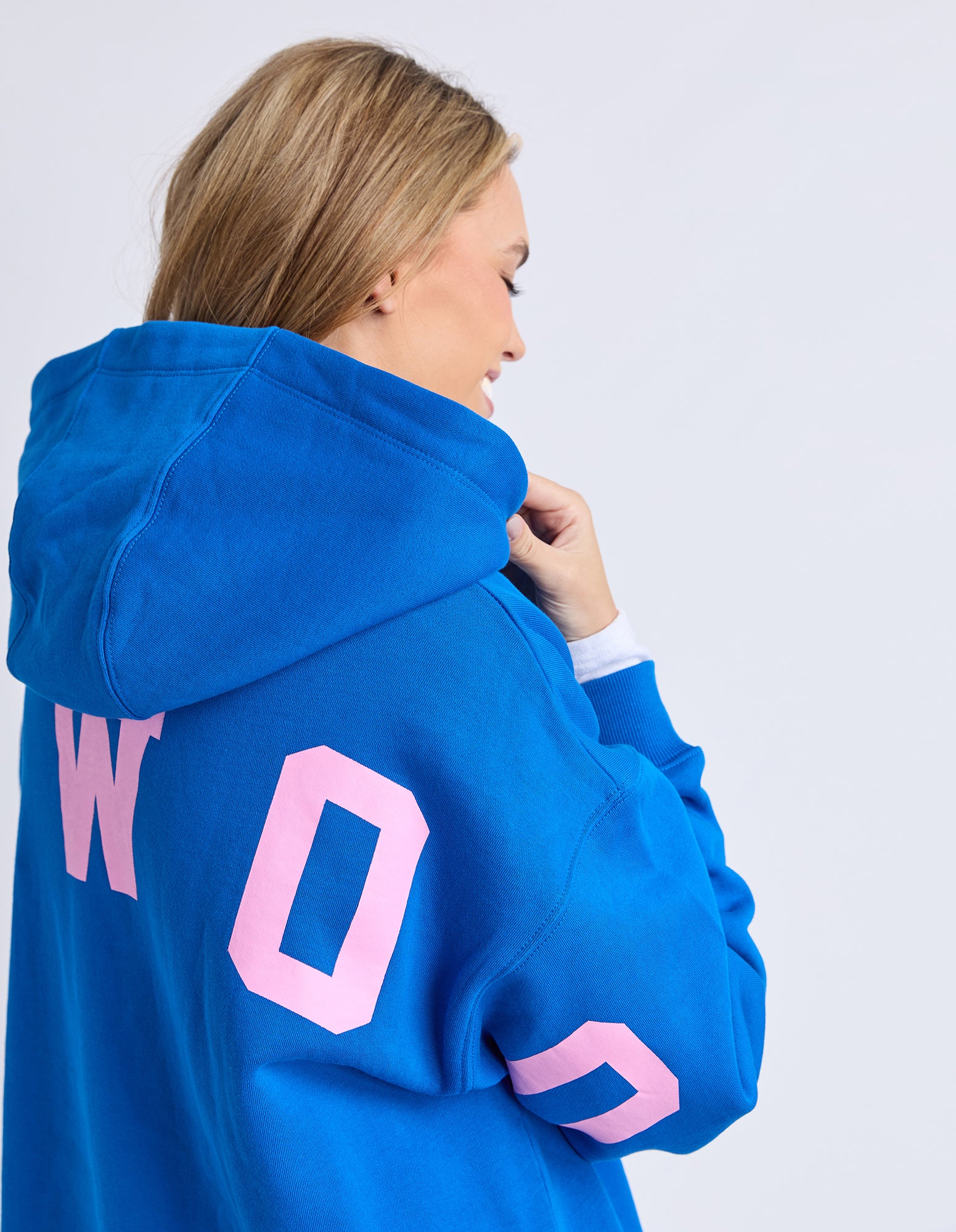 Woman wearing a blue Foxwood hoodie with pink letters on a white background
