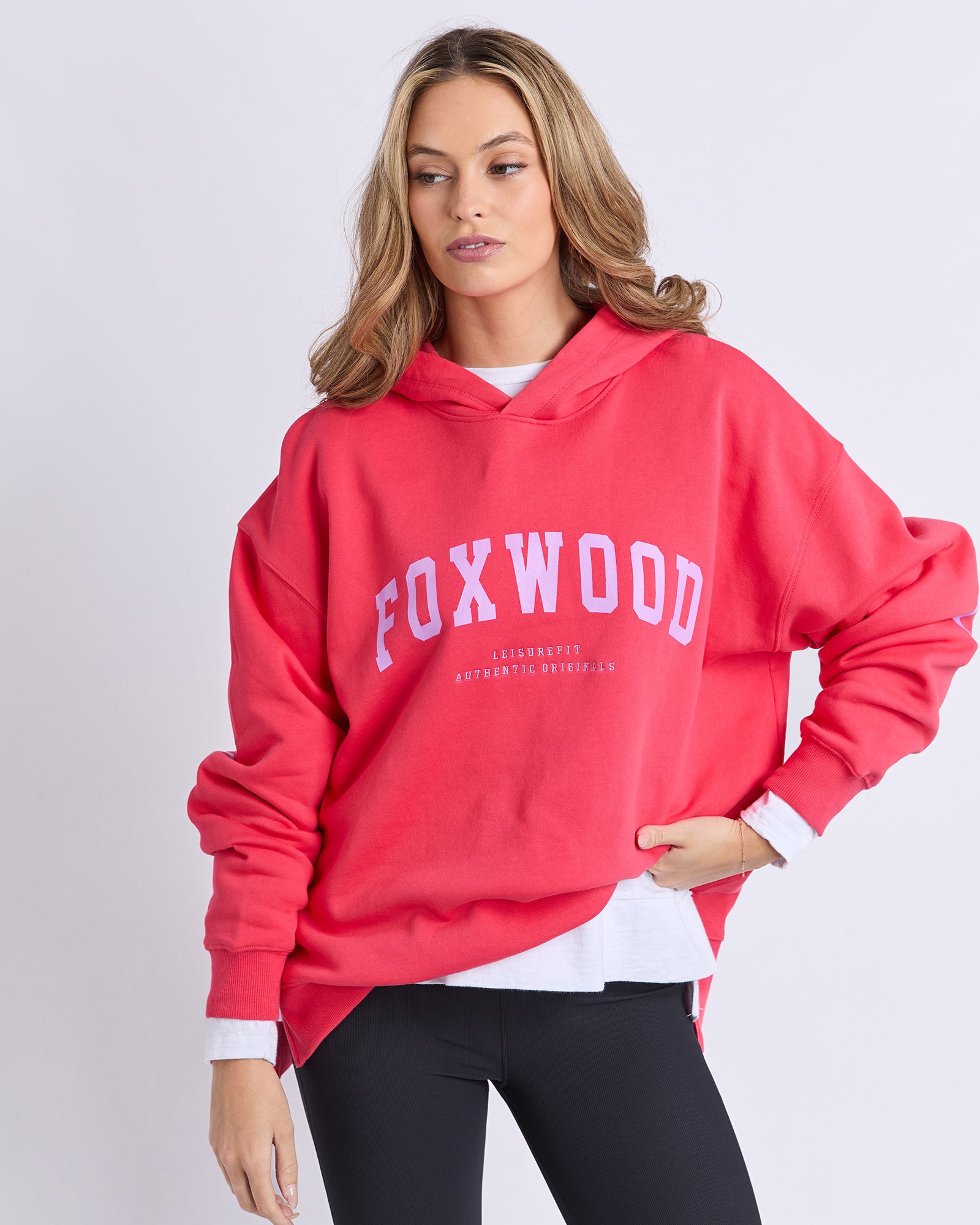 Woman wearing a red 'FOXWOOD' hoodie  with purple print on a light grey background