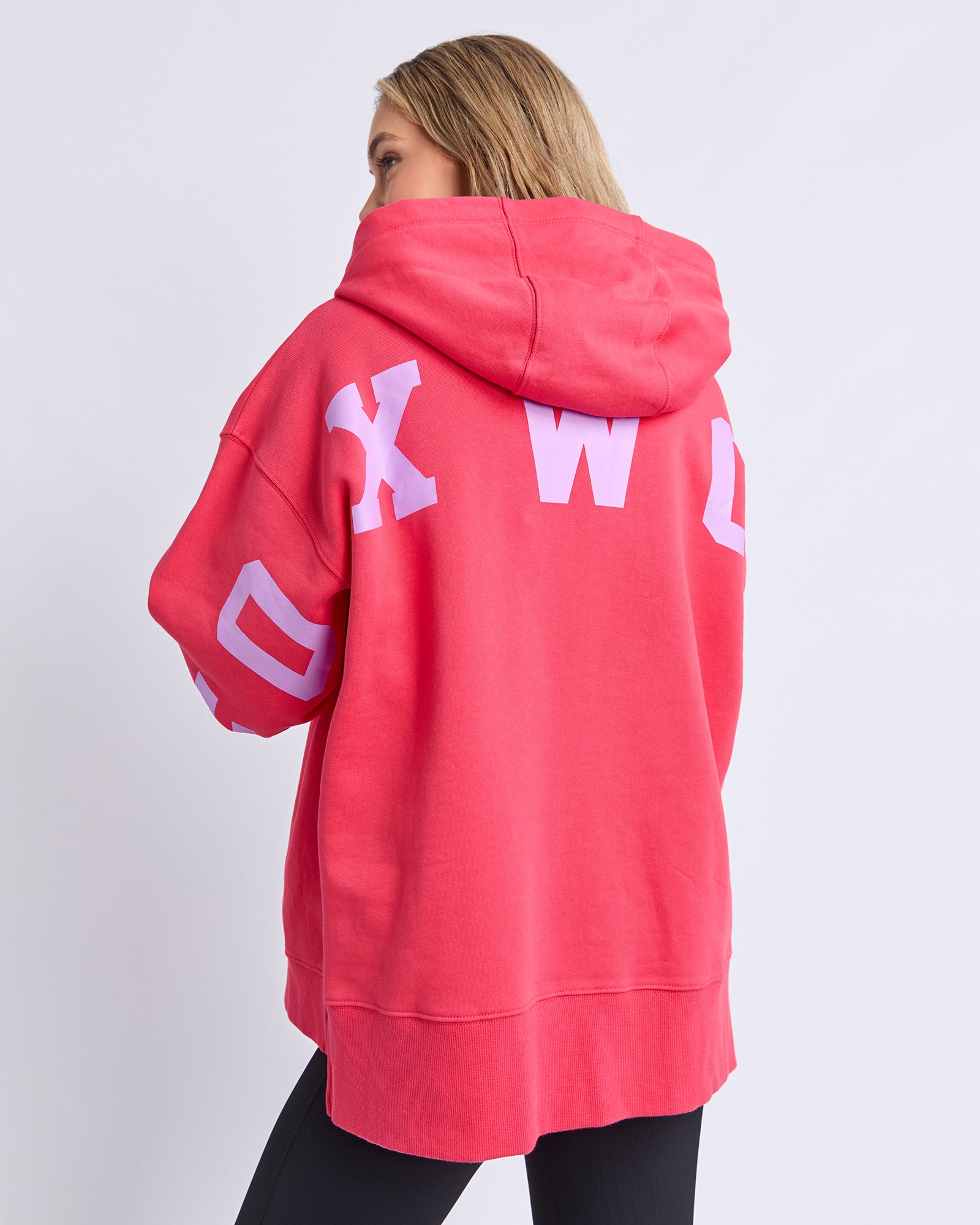 Woamn wearing a Foxwood raspberry hoodie with white text on the back against a light grey background