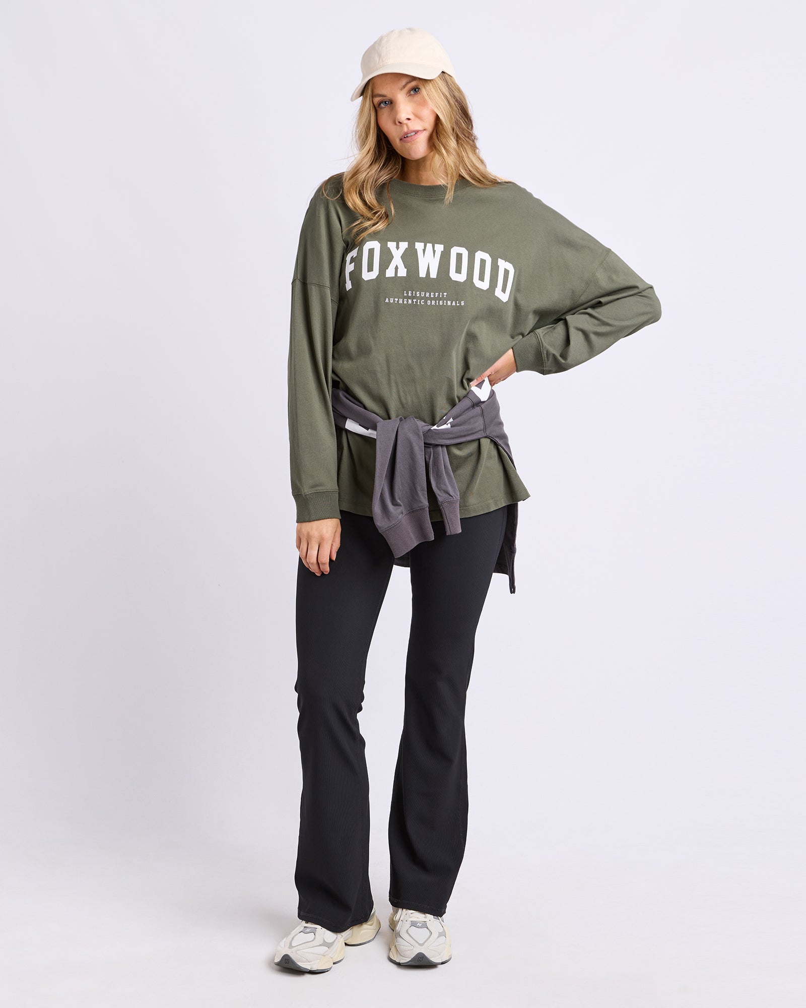 Image of Woman wearing a khaki 'Foxwood' long sleeve tee with black pants on a light grey background