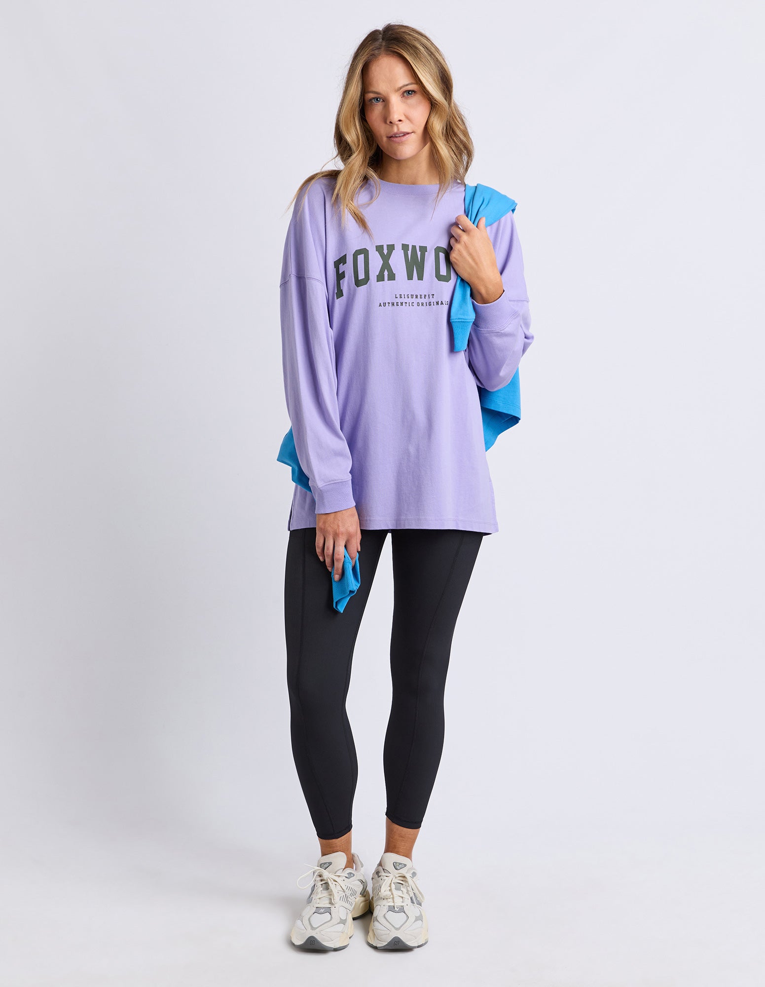 Woman wearing a purple 'FOXWOOD' long sleeve tee with writing in khaki and black leggings on a white background