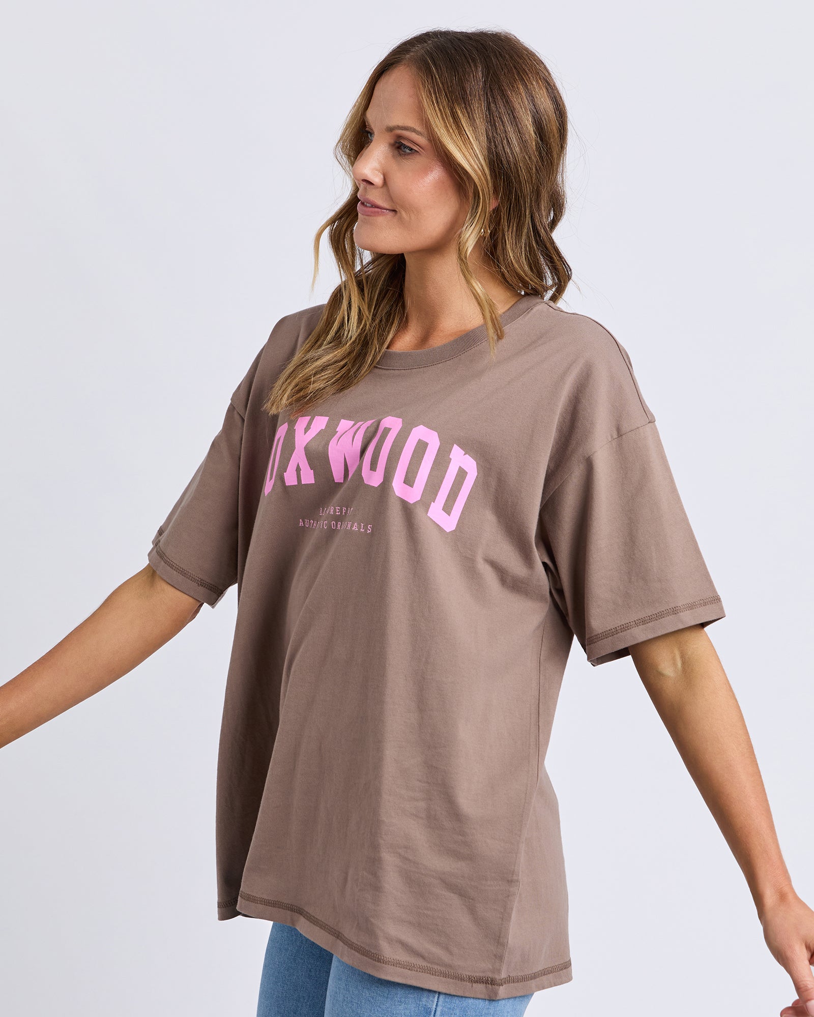 Image of Woman wearing a Foxwood brown t-shirt with pink text on a plain background